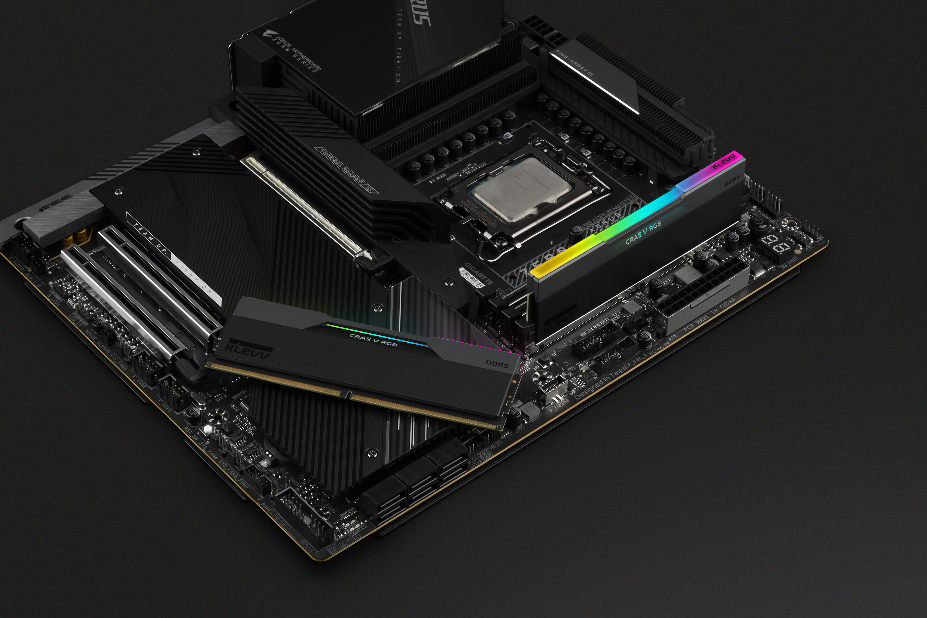 A computer motherboard with RAM sticks, and a CPU, all on a black surface.