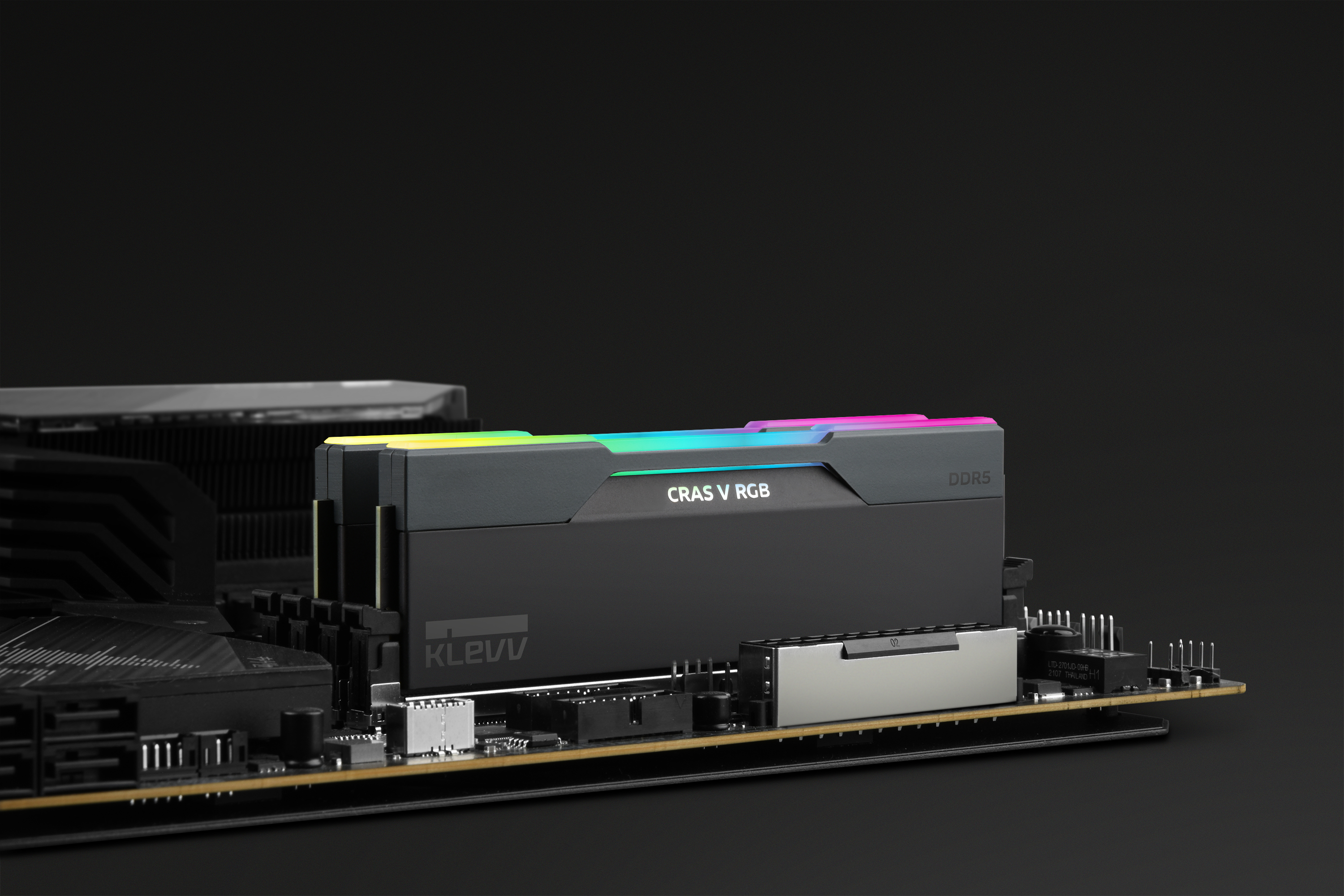 A close-up of a black RAM stick with RGB lighting, mounted on a motherboard. The background is black.