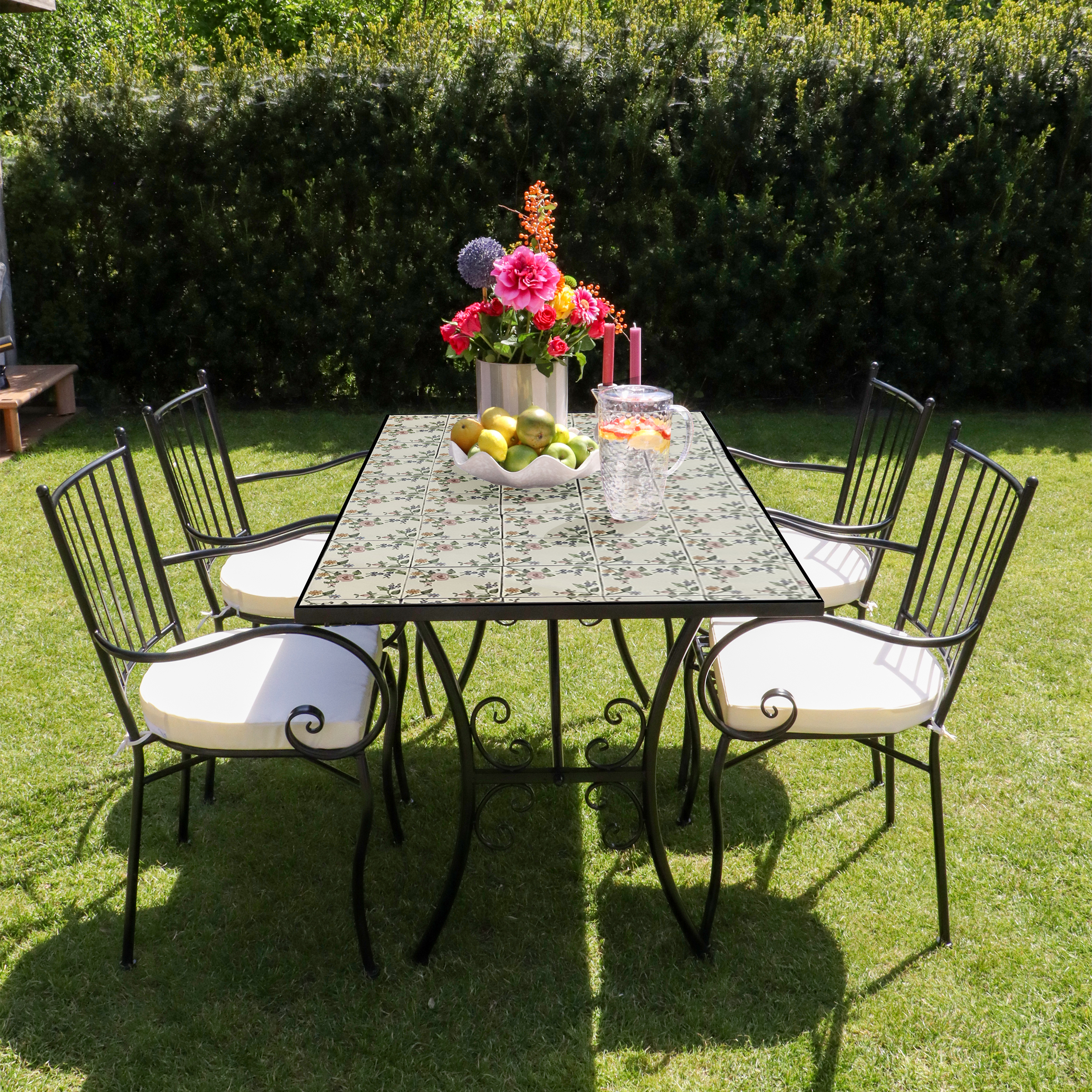Ein Tisch mit Blumen, Früchten und Getränken ist für ein Abendessen im Freien mit Stühlen auf grünem Gras in der Sonne gedeckt.
