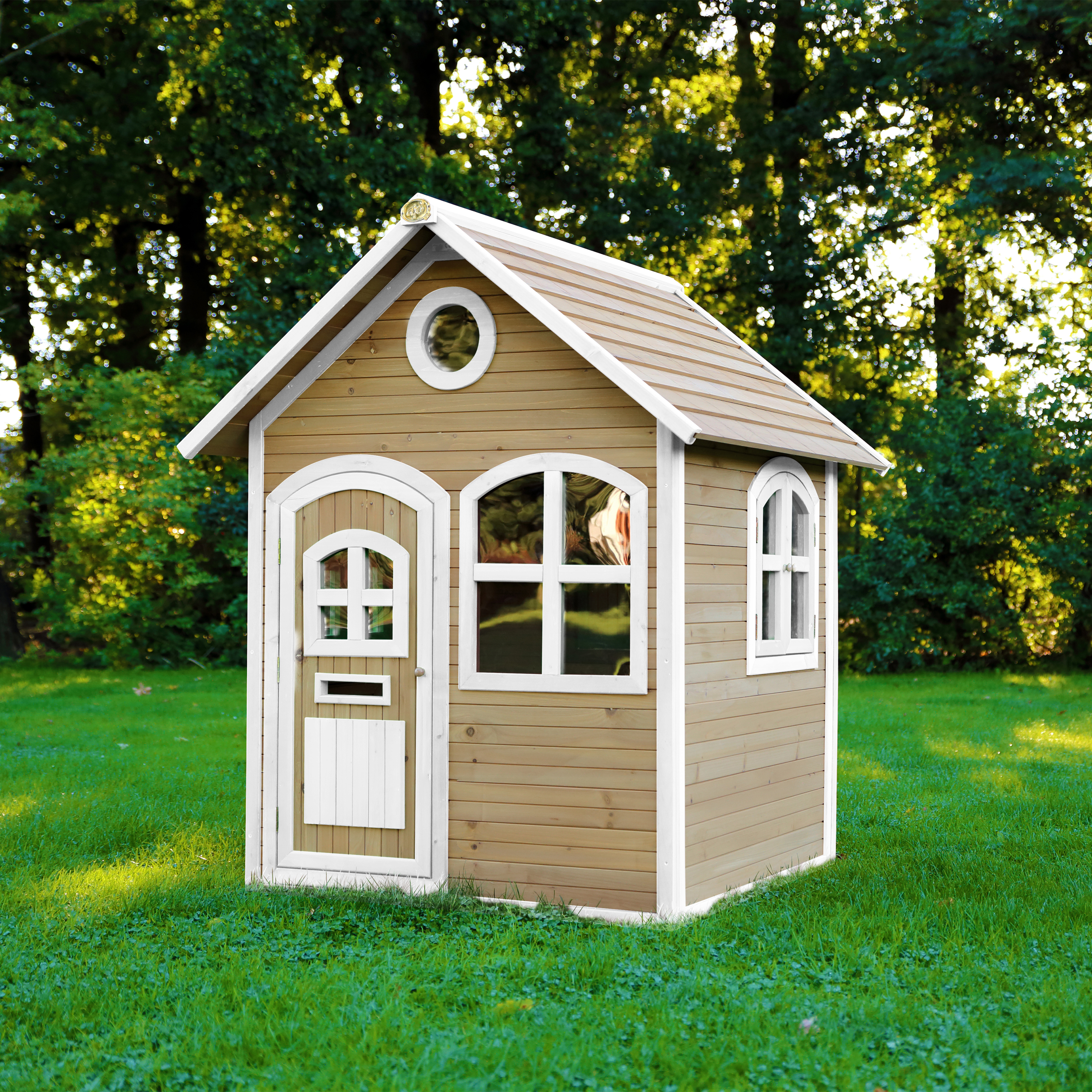 Ein hölzernes Spielhaus mit weißer Verkleidung steht auf grünem Gras. Bäume bilden den Hintergrund.