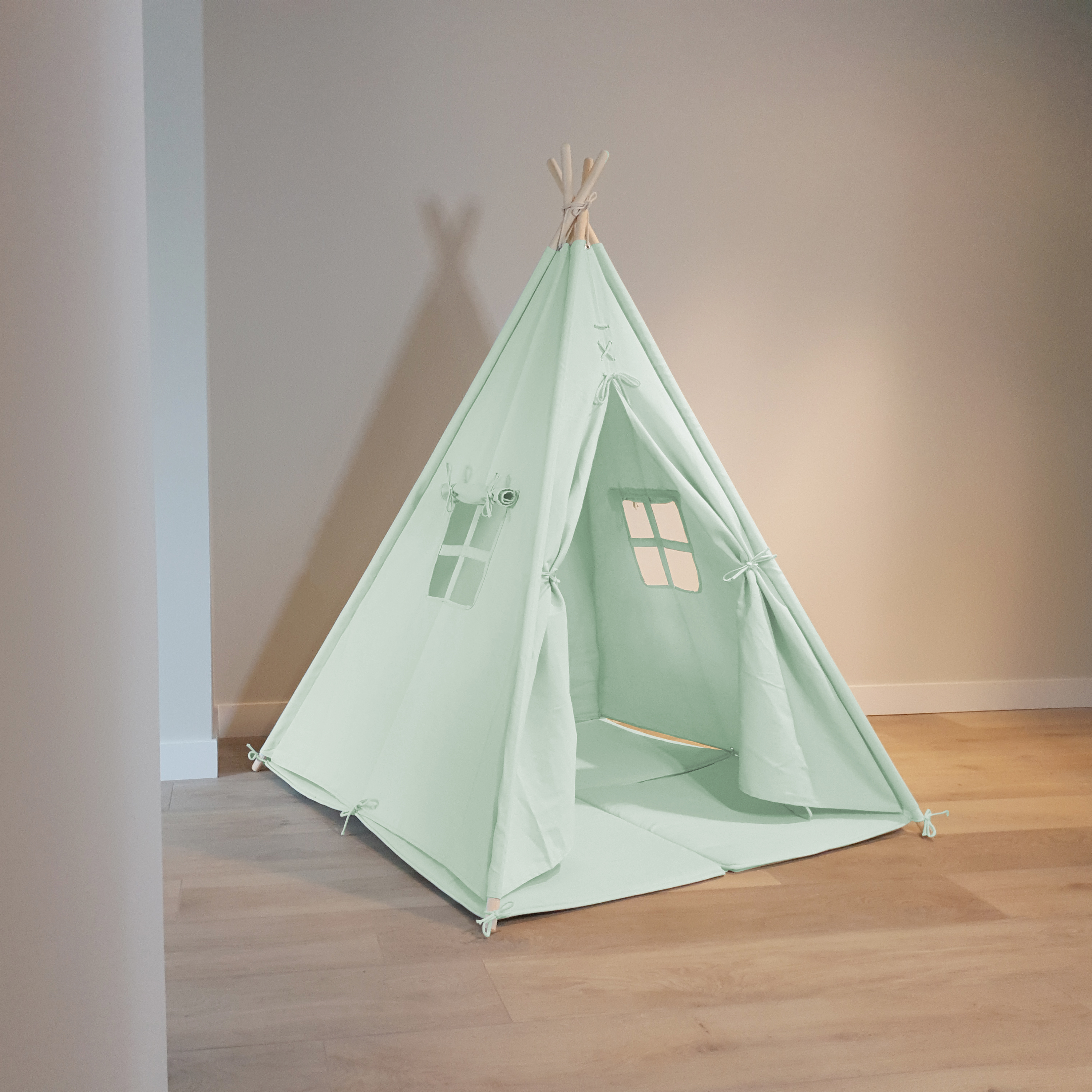 Ein mintgrünes Tipi-Zelt steht auf einem Holzboden, mit zwei kleinen Fenstern und neutralem Hintergrund.