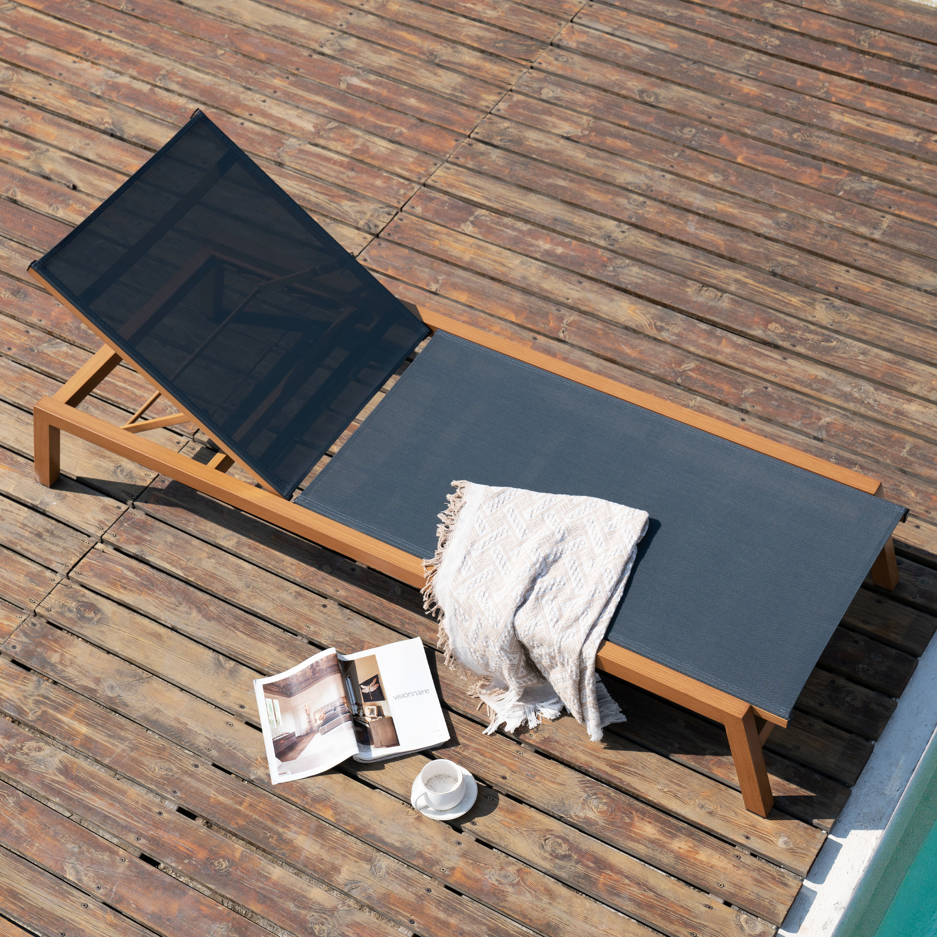 Eine Liege mit Decke und Zeitschrift auf einem Holzdeck neben einem Pool.