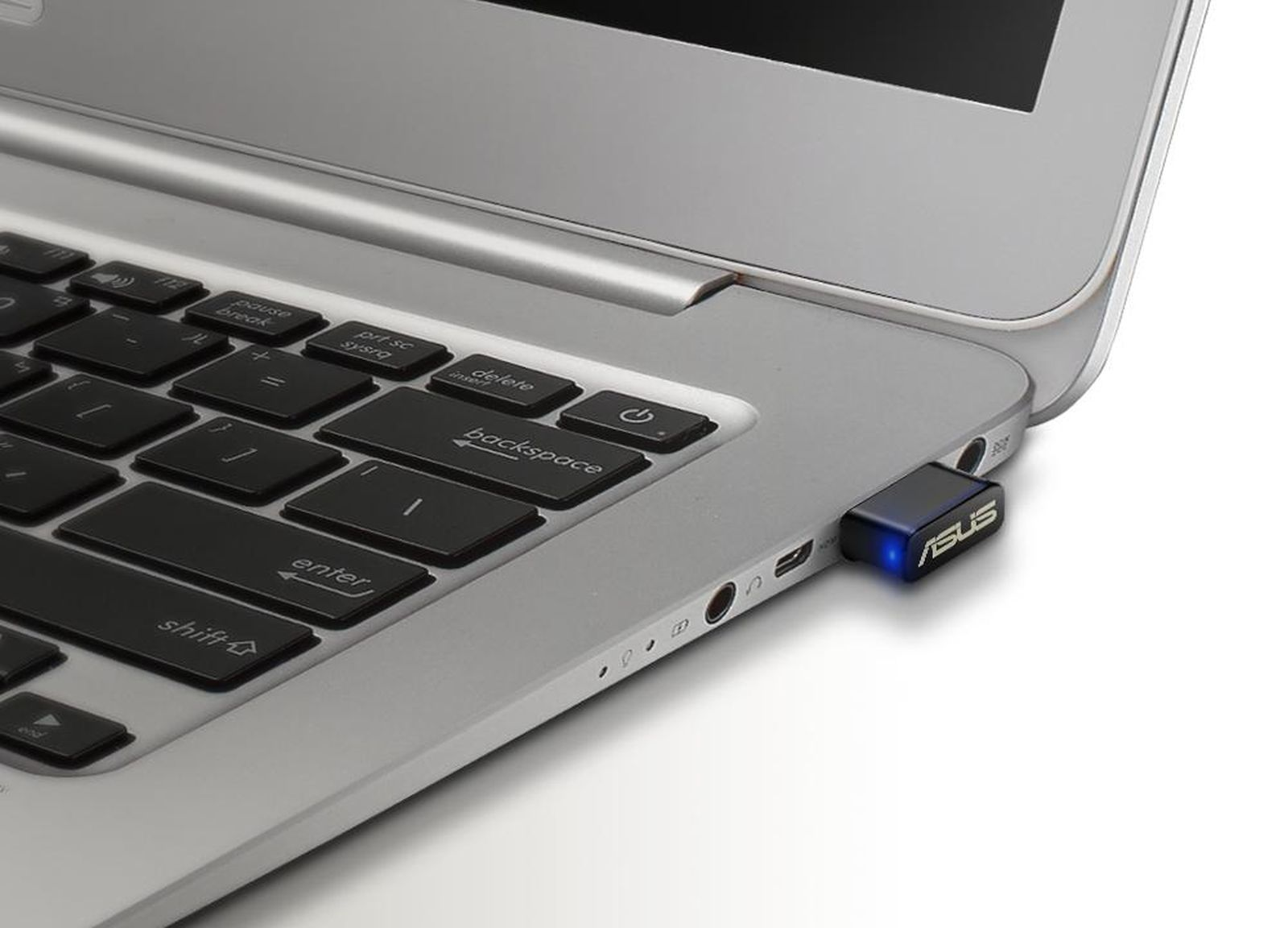 Laptop-Tastatur mit schwarzen Tasten und silbernem Rahmen. Ein ASUS USB-Dongle ist eingesteckt. Der Power-Knopf ist an.