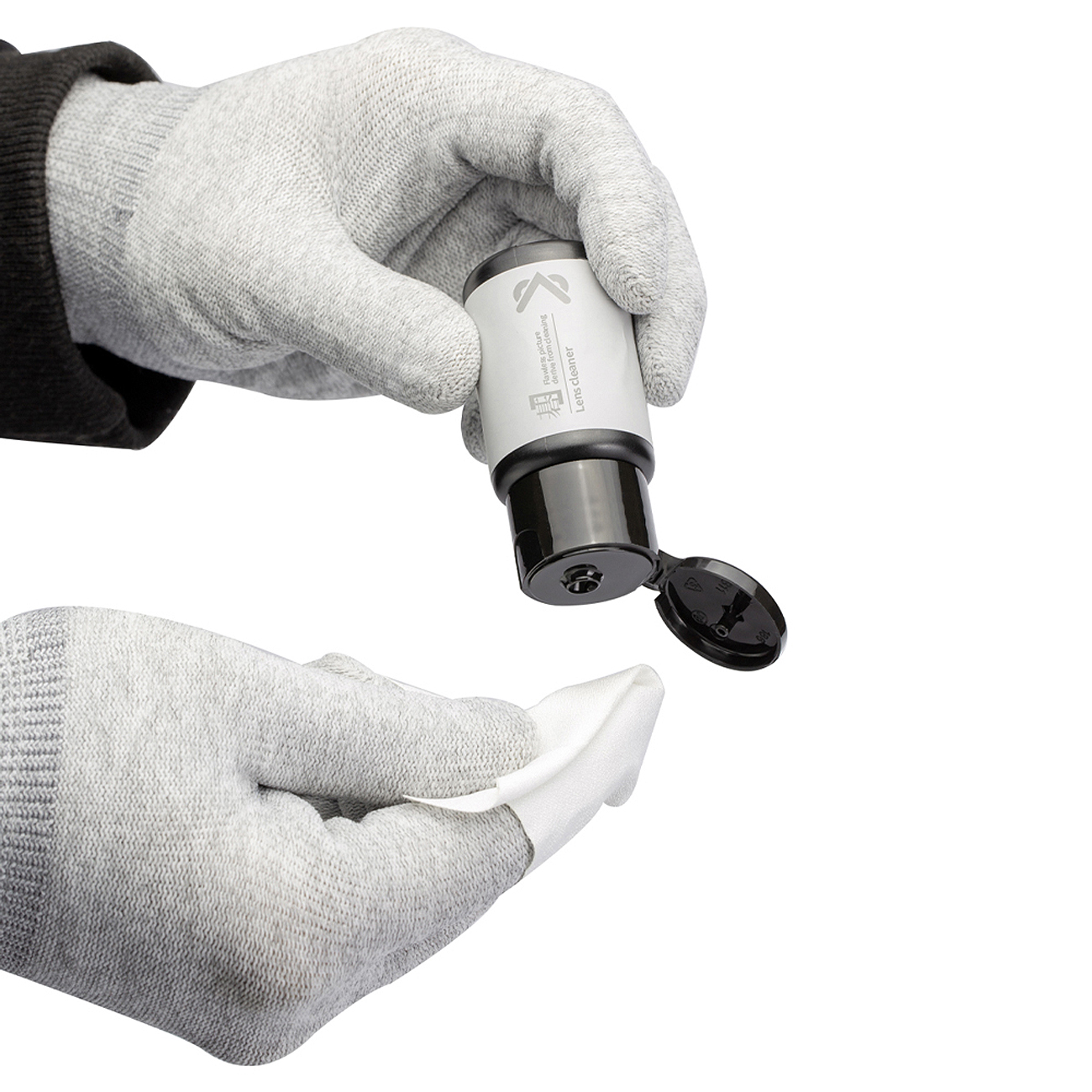 Hände in grauen Handschuhen halten einen Linsenreiniger und ein weißes Tuch. Der Linsenreiniger ist schwarz und weiß, die Kappe ist offen.