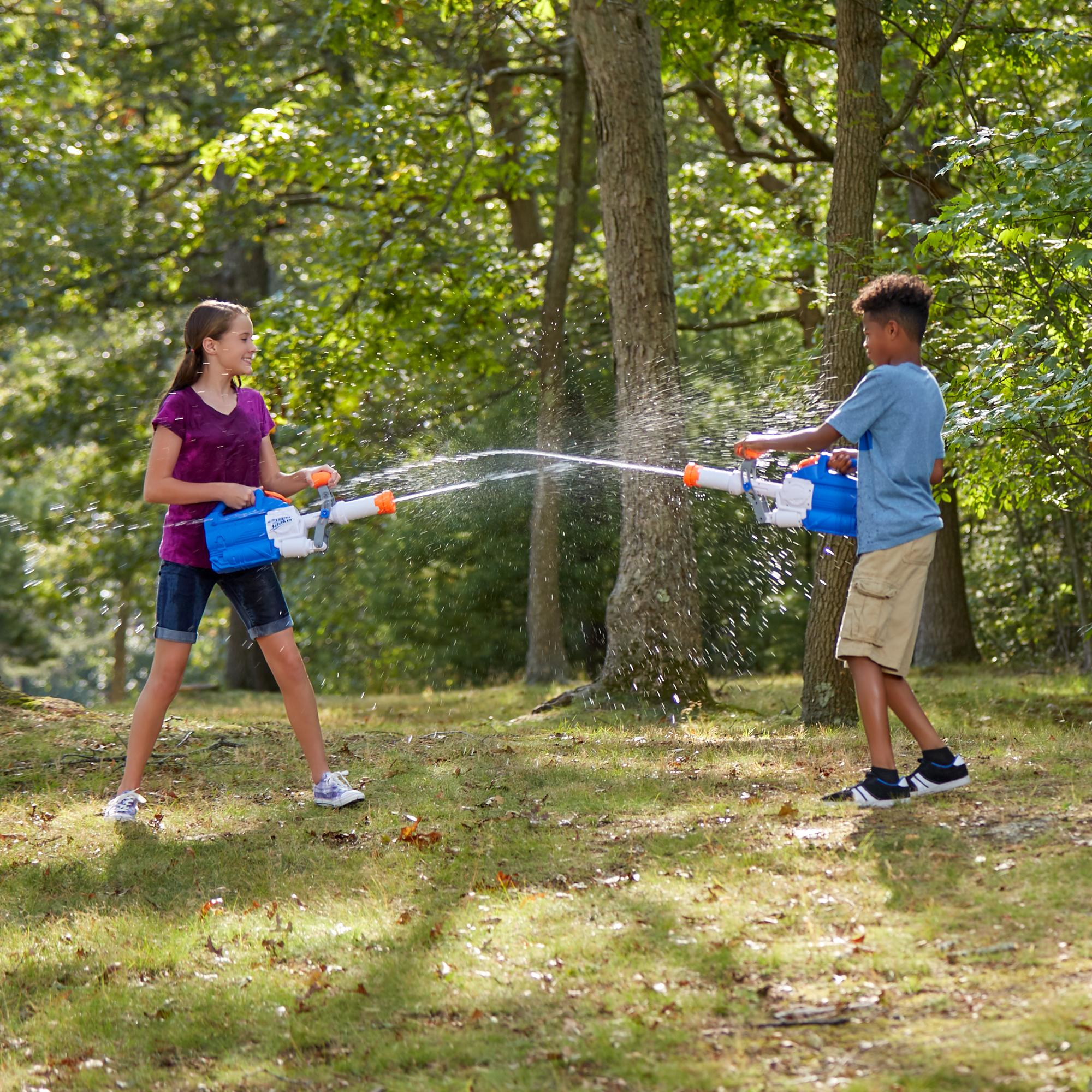 Due bambini giocano con pistole ad acqua in un parco. L'acqua sgorga dalle pistole. Alberi ed erba sullo sfondo.