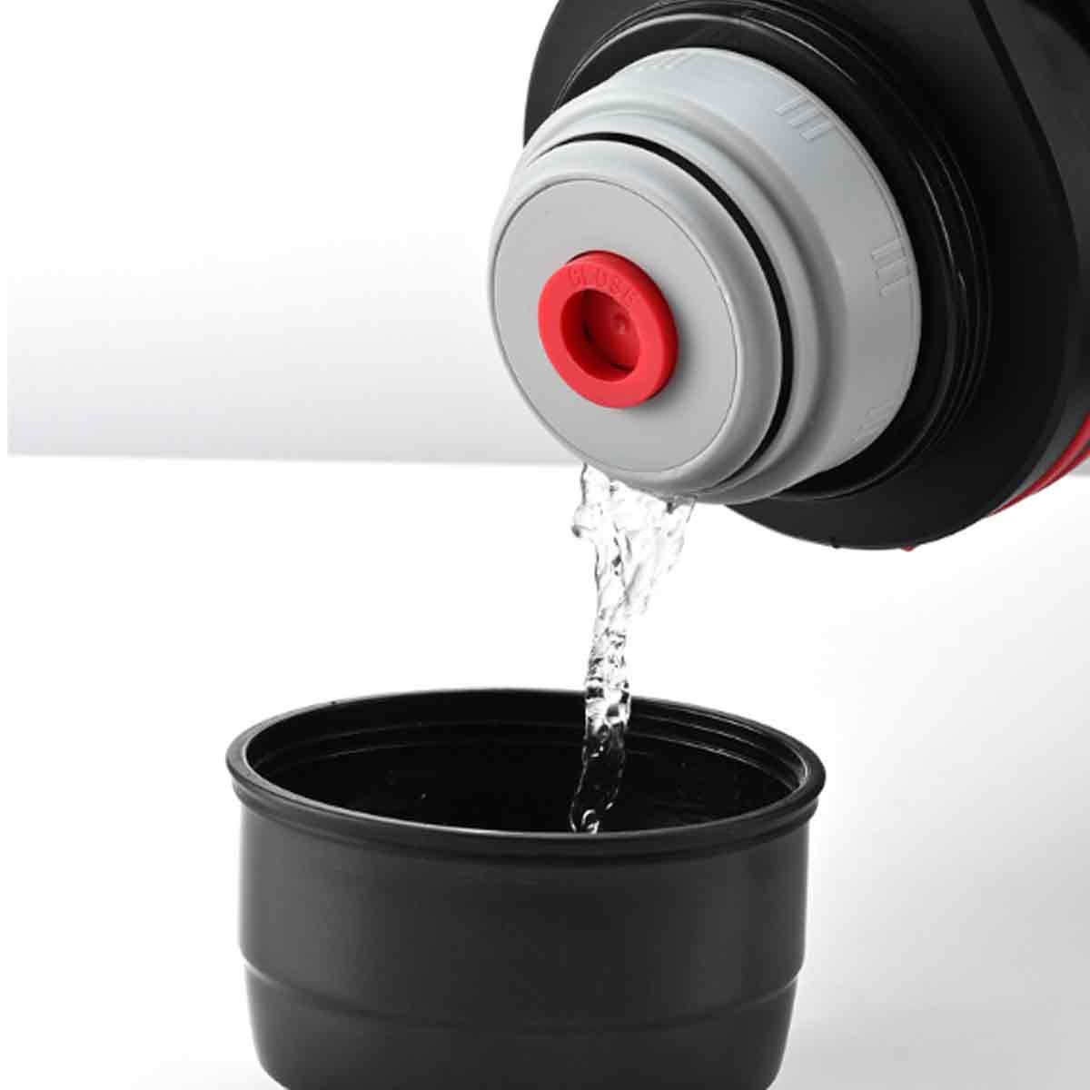 Ein schwarzer Thermosbehälter gießt Wasser in eine schwarze Tasse. Der Thermosbehälter hat einen rot-grauen Deckel mit der Aufschrift „Close“.