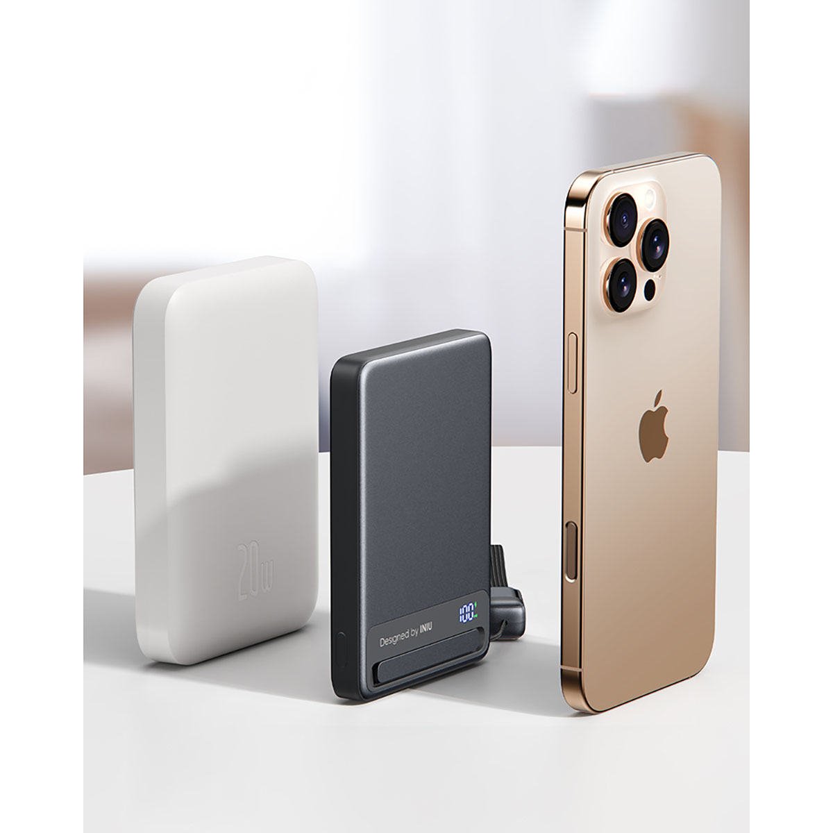 L'image montre une batterie externe blanche, une batterie externe noire et un iPhone doré. Le tout sur une surface blanche.