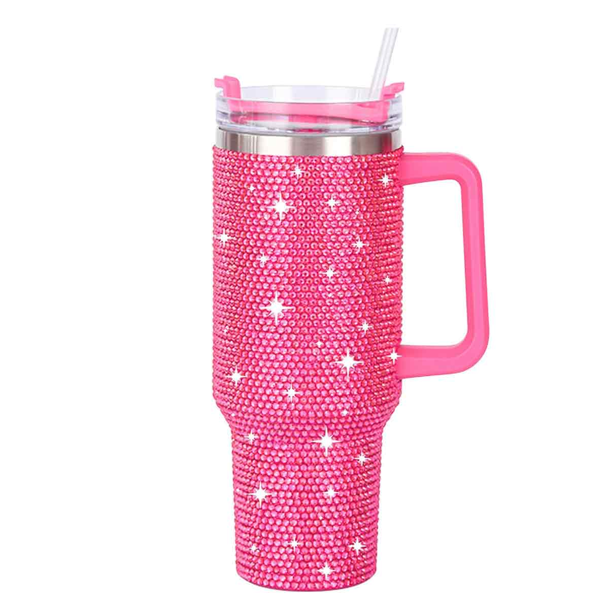 Ein pinkfarbener, mit Glitzersteinen besetzter Becher mit Griff, Deckel und Strohhalm. Weiße Sternverzierungen sind verstreut.