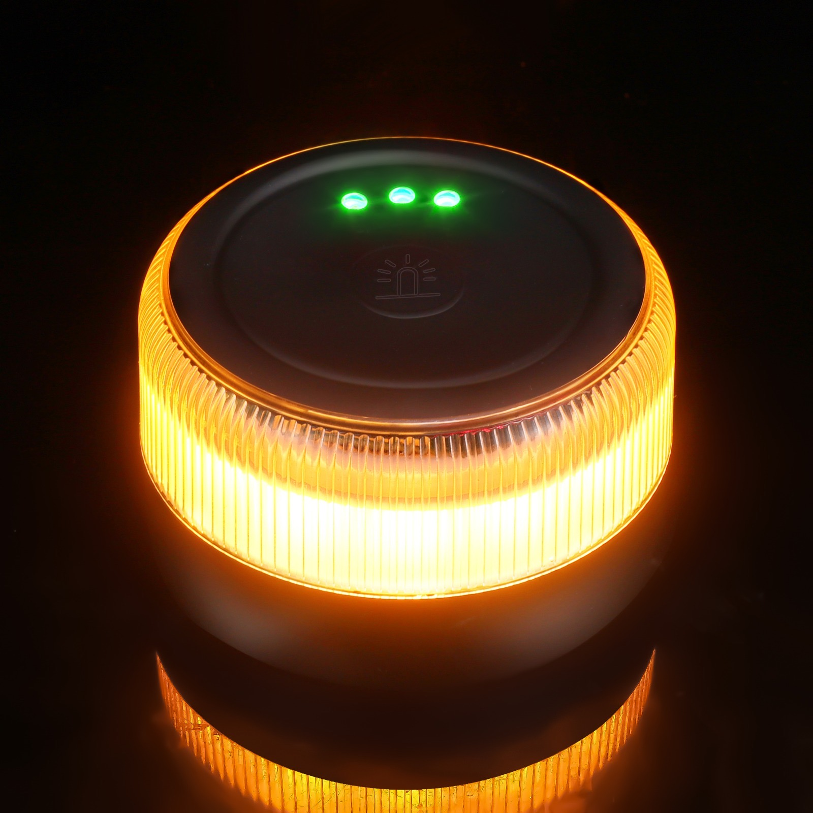 Un dispositivo redondo, naranja y encendido con tres luces verdes en la parte superior. Está sobre una superficie oscura y refleja.