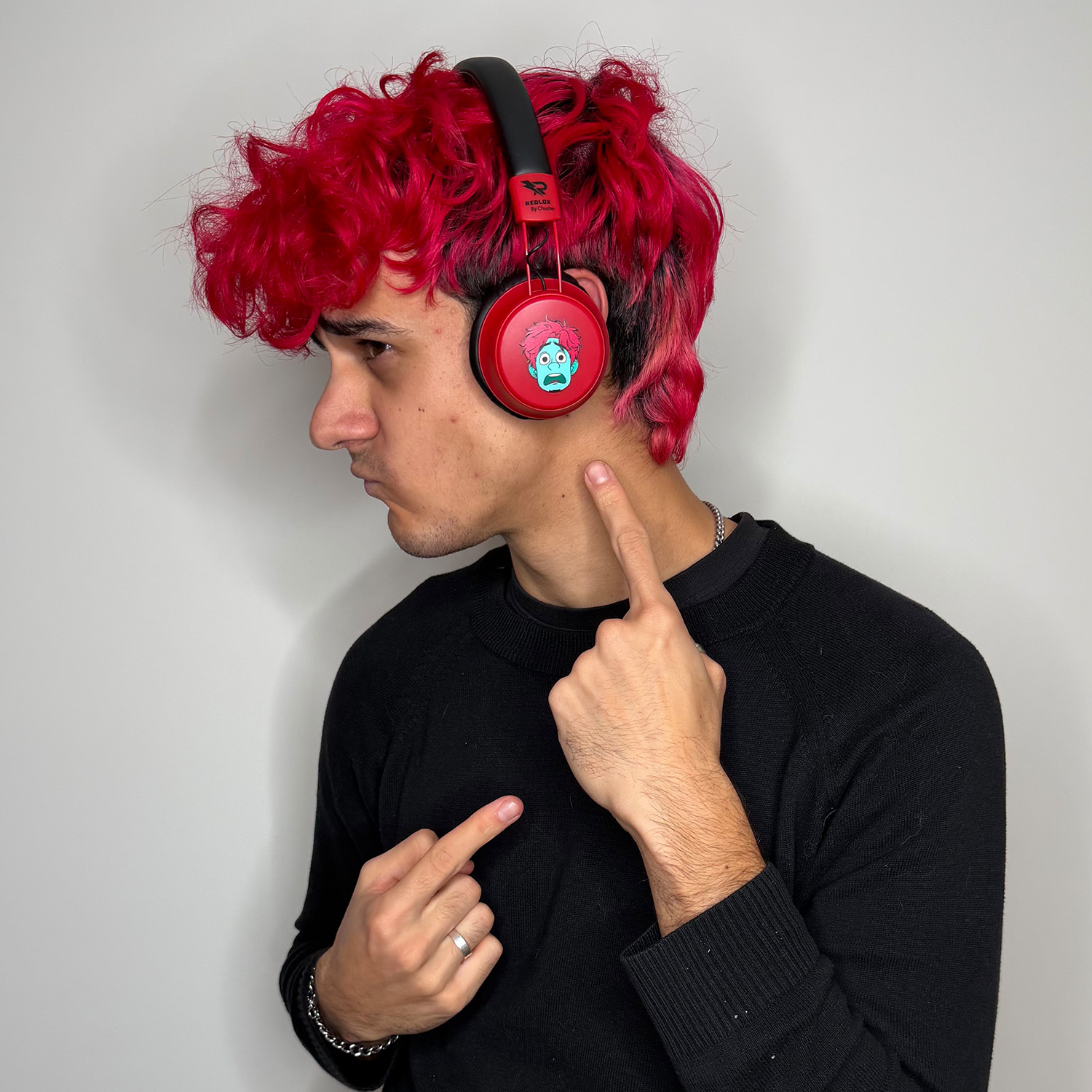 Un uomo con i capelli rossi che indossa le cuffie indica il collo. Indossa un maglione nero. Le cuffie hanno un volto di cartone animato.