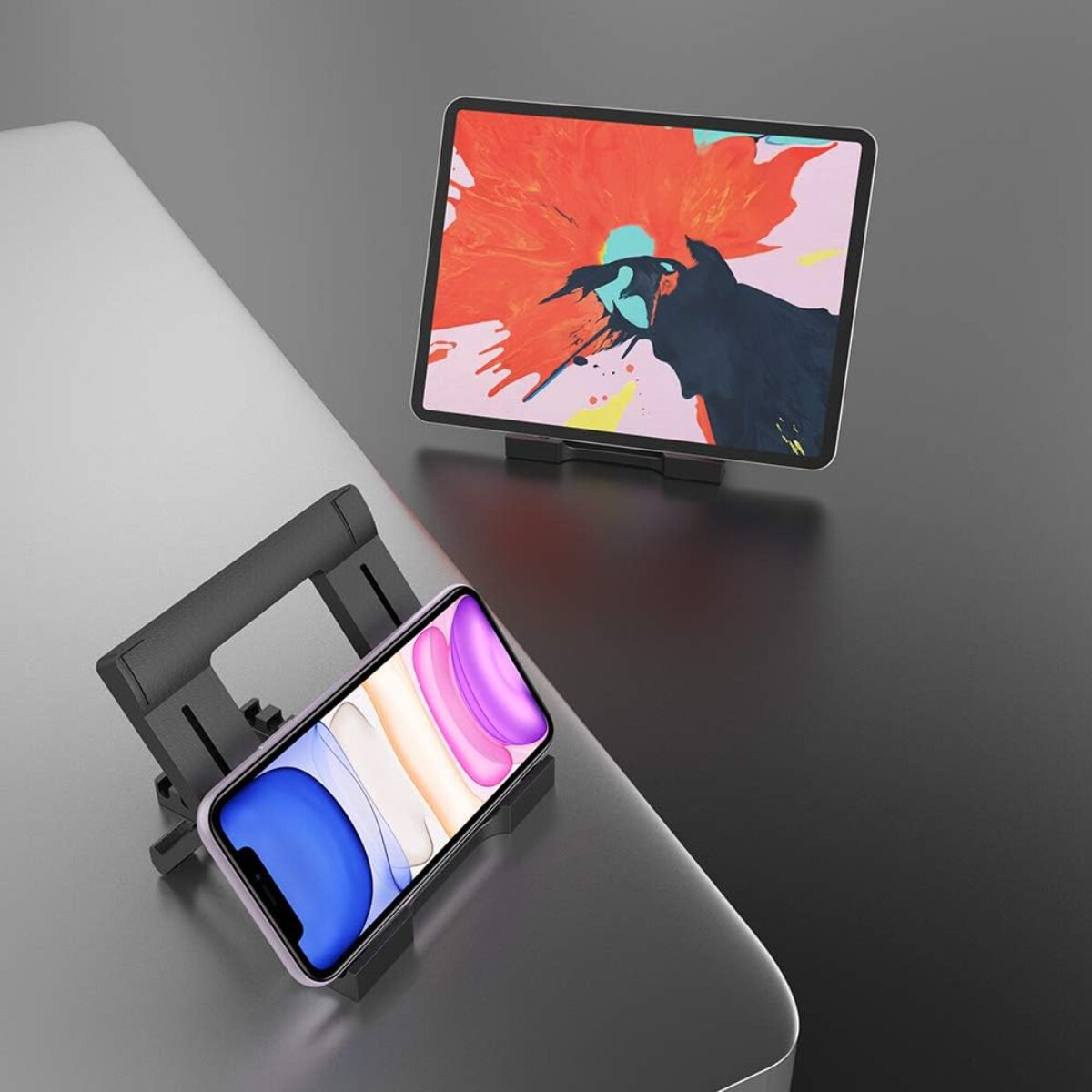 Ein Telefon und ein Tablet stehen auf Ständern. Das Tablet zeigt farbenfrohe abstrakte Kunst. Der Bildschirm des Telefons zeigt einen Farbverlauf.