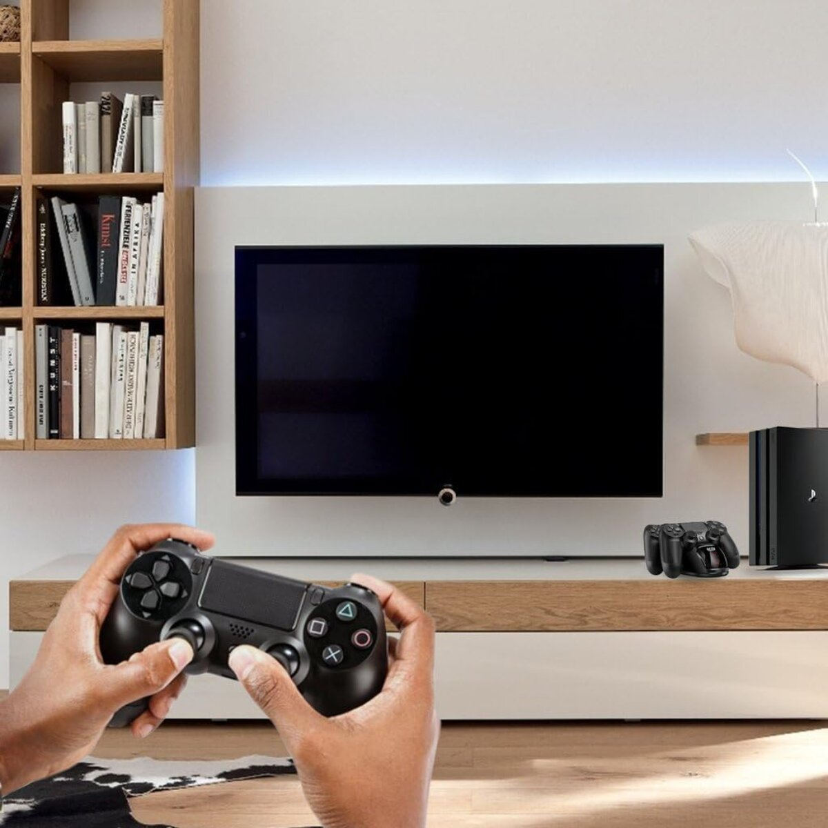 Hände halten einen schwarzen Gamecontroller vor einem Fernseher. Ein Regal mit Büchern und eine Spielkonsole sind sichtbar.