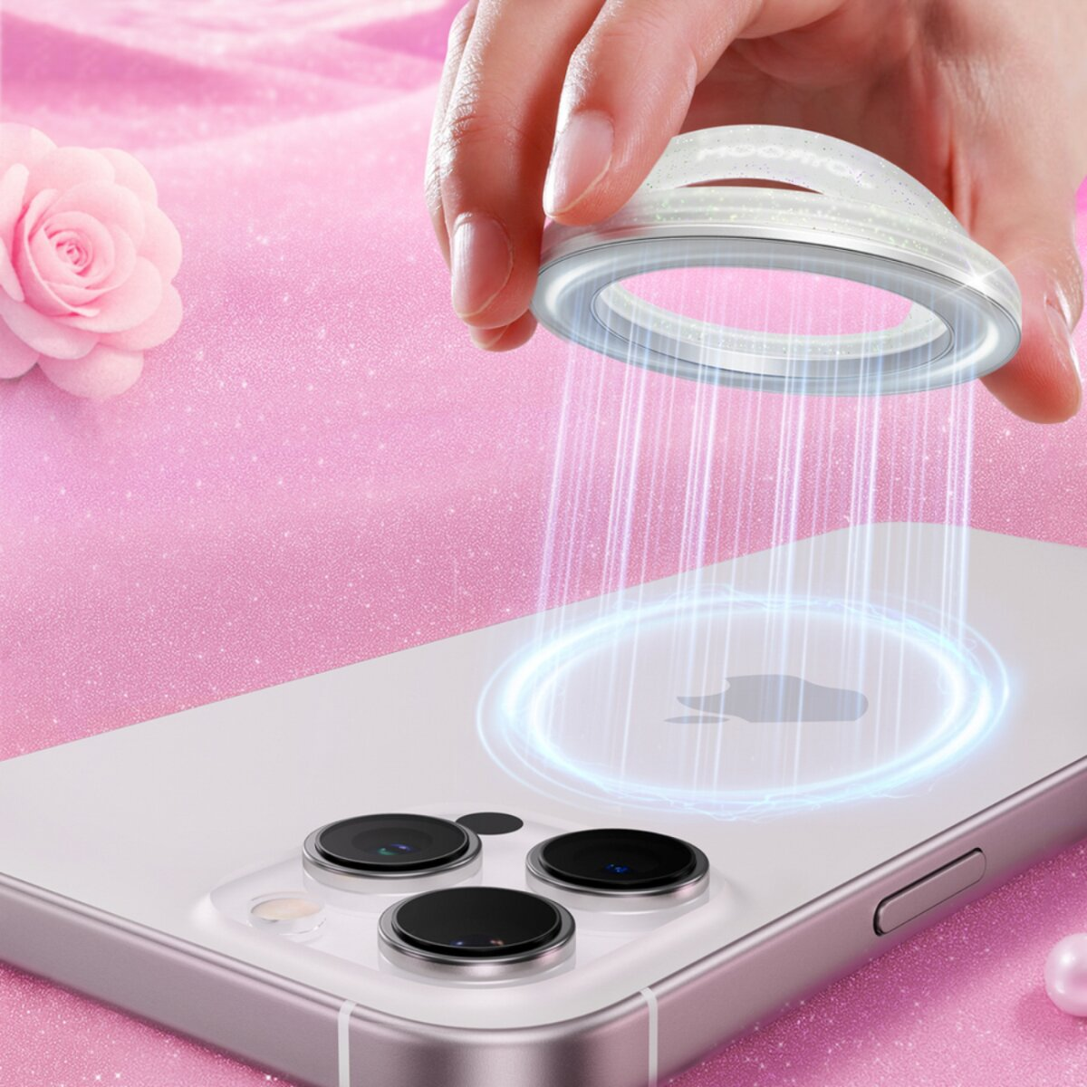 Hand hält ringförmiges Gerät über Telefon. Telefon hat drei Kameralinsen. Rosa Hintergrund mit Rose und Glitzer.