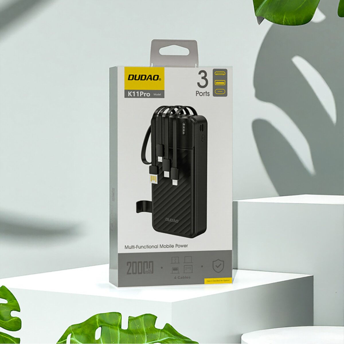 Power bank DUDAO K11Pro nera in scatola con cavi. Ha 3 porte e capacità di 20000mAh. Foglie verdi in primo e secondo piano.