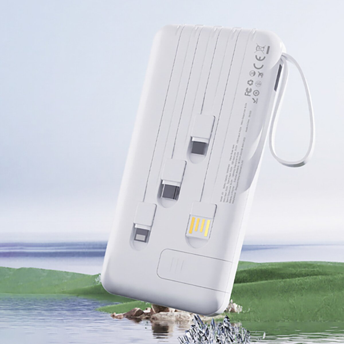 Un power bank bianco con più porte di ricarica, un'impugnatura ad anello, su uno sfondo sfocato di acqua e colline verdi.