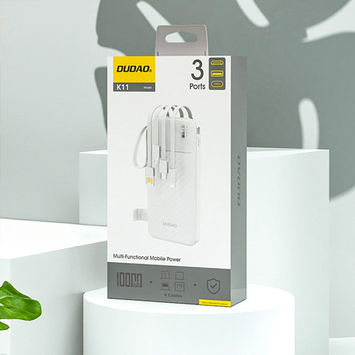 Una scatola bianca di power bank DUDOA. Ha 3 porte e 4 cavi. La scatola  è su una piattaforma bianca con foglie verdi.