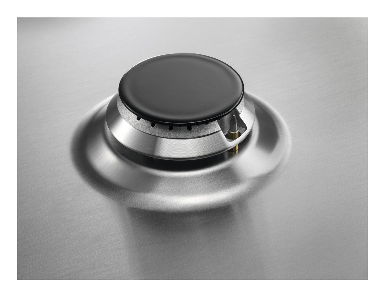 Zbliżenie na palnik gazowy ze stali nierdzewnej. Czarny, okrągły palnik znajduje się na srebrnej podstawie. Tło to również szczotkowana stal.