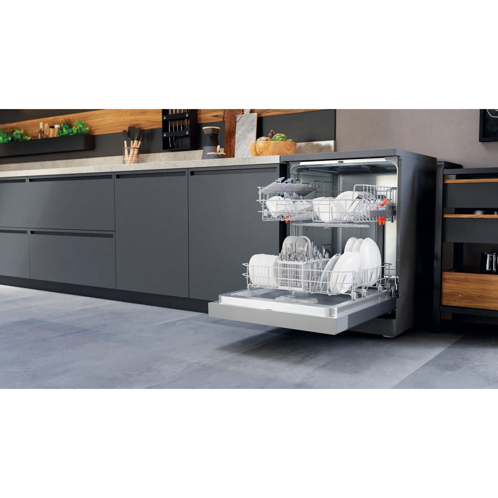 Un lavavajillas con la puerta abierta, cargado de platos, está en una cocina moderna. Se ven armarios gris oscuro y suelo gris claro.