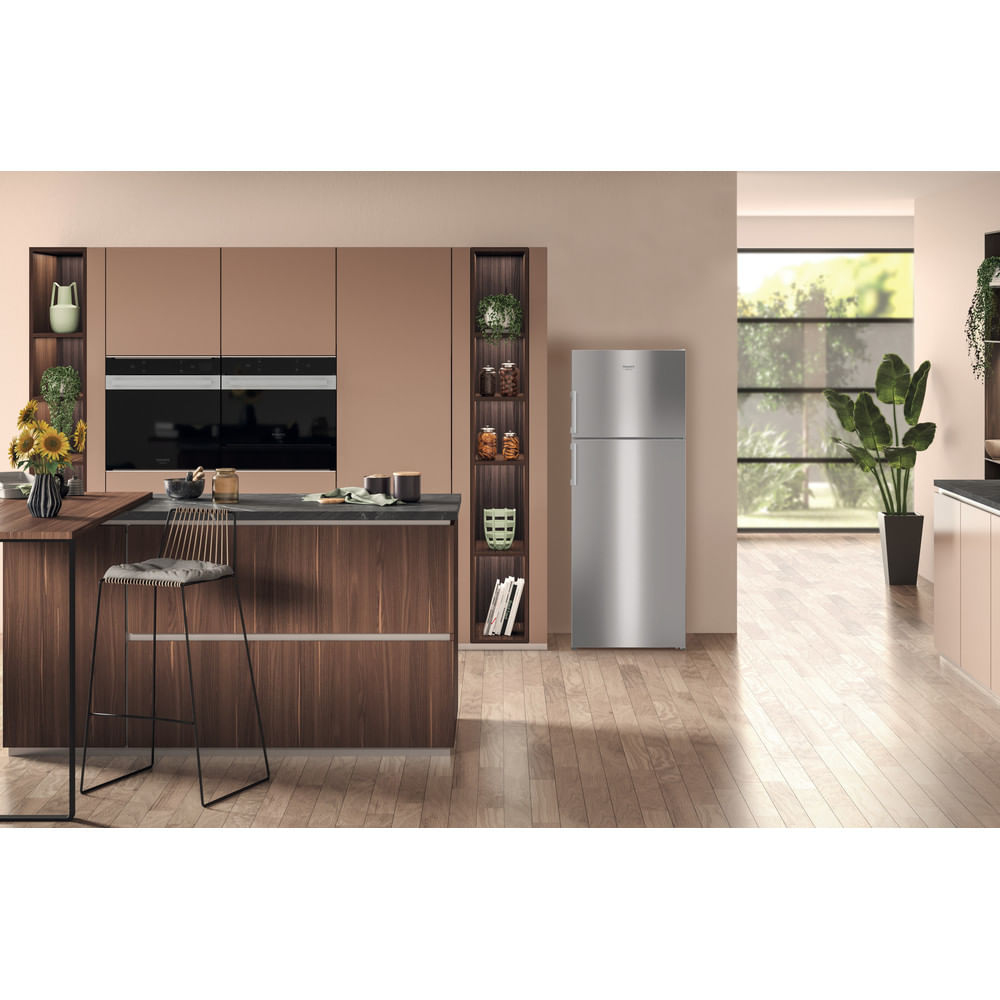 Una cucina moderna con un frigorifero in acciaio inossidabile, mobili in legno e uno sgabello da bar. Presenti anche una pianta e dei fiori.