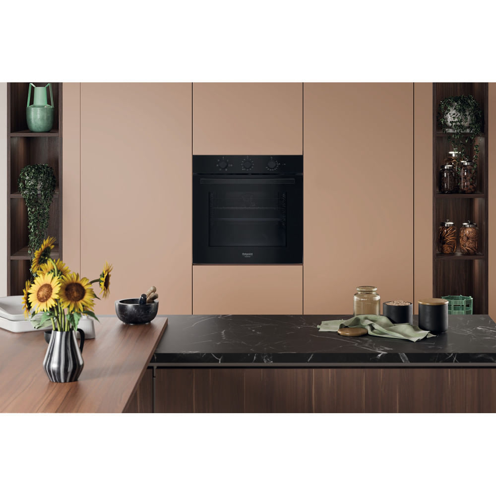 Scena di cucina con forno, girasoli e barattoli sugli scaffali. Piano di lavoro nero e armadi in legno visibili.