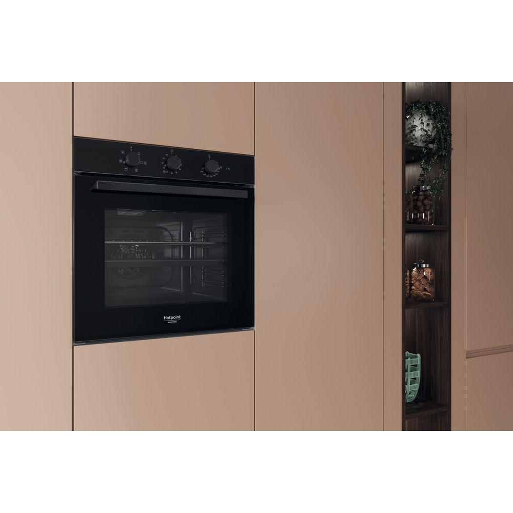 Una cucina moderna con forno nero a incasso. Accanto, una mensola in legno con piante e barattoli. Armadi beige circondano il forno.