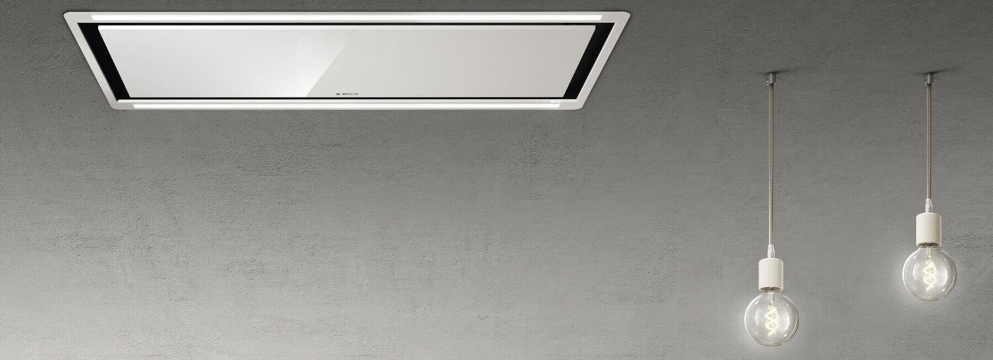 Cappa rettangolare bianca su muro grigio. Due lampade a sospensione con lampadine Edison sono sotto.