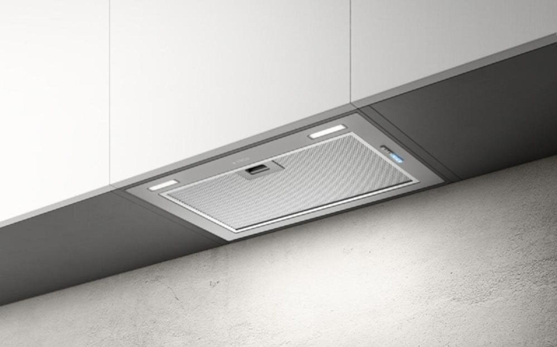 Una moderna cappa da cucina montata sotto un mobile bianco. Grigia, con luci e filtro a rete, contro un muro strutturato.