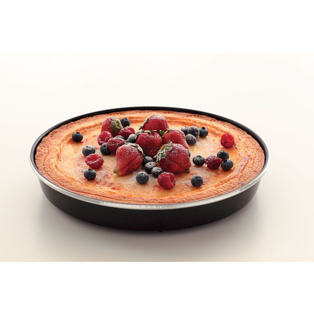 Una cheesecake rotonda in una padella nera, guarnita con fragole, mirtilli e lamponi. Lo sfondo è bianco.