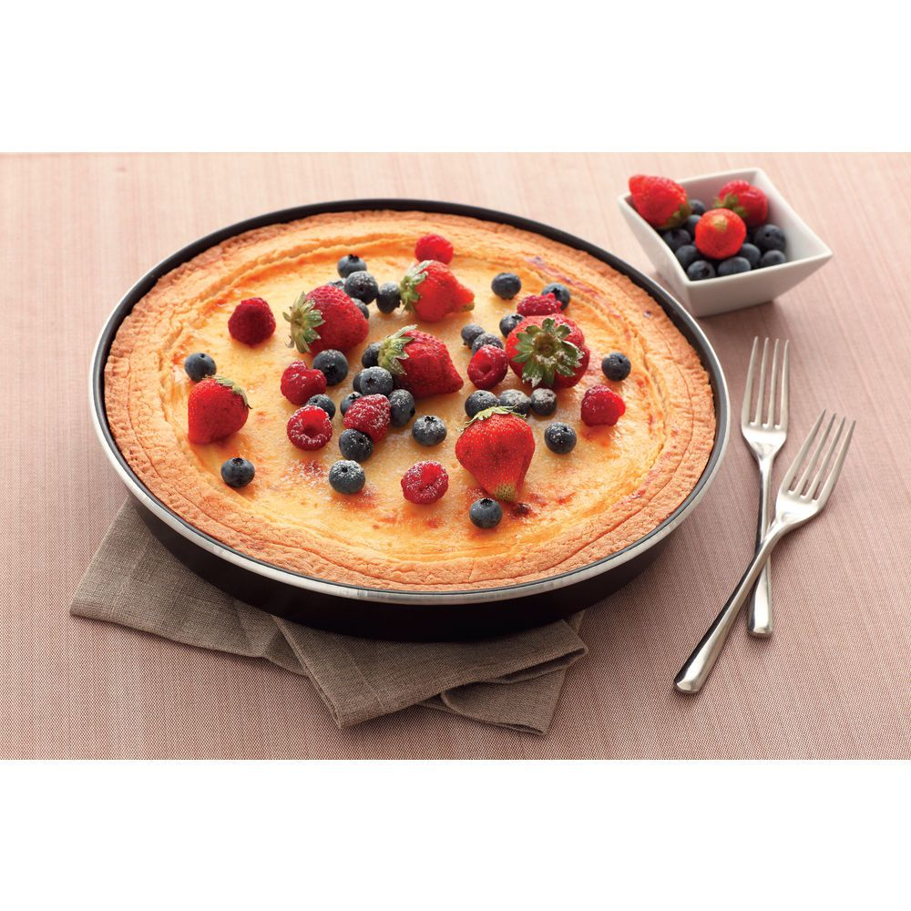 Una crostata cotta in padella, guarnita con fragole, mirtilli e lamponi. Forchette e una ciotola di frutti di bosco sono a lato.