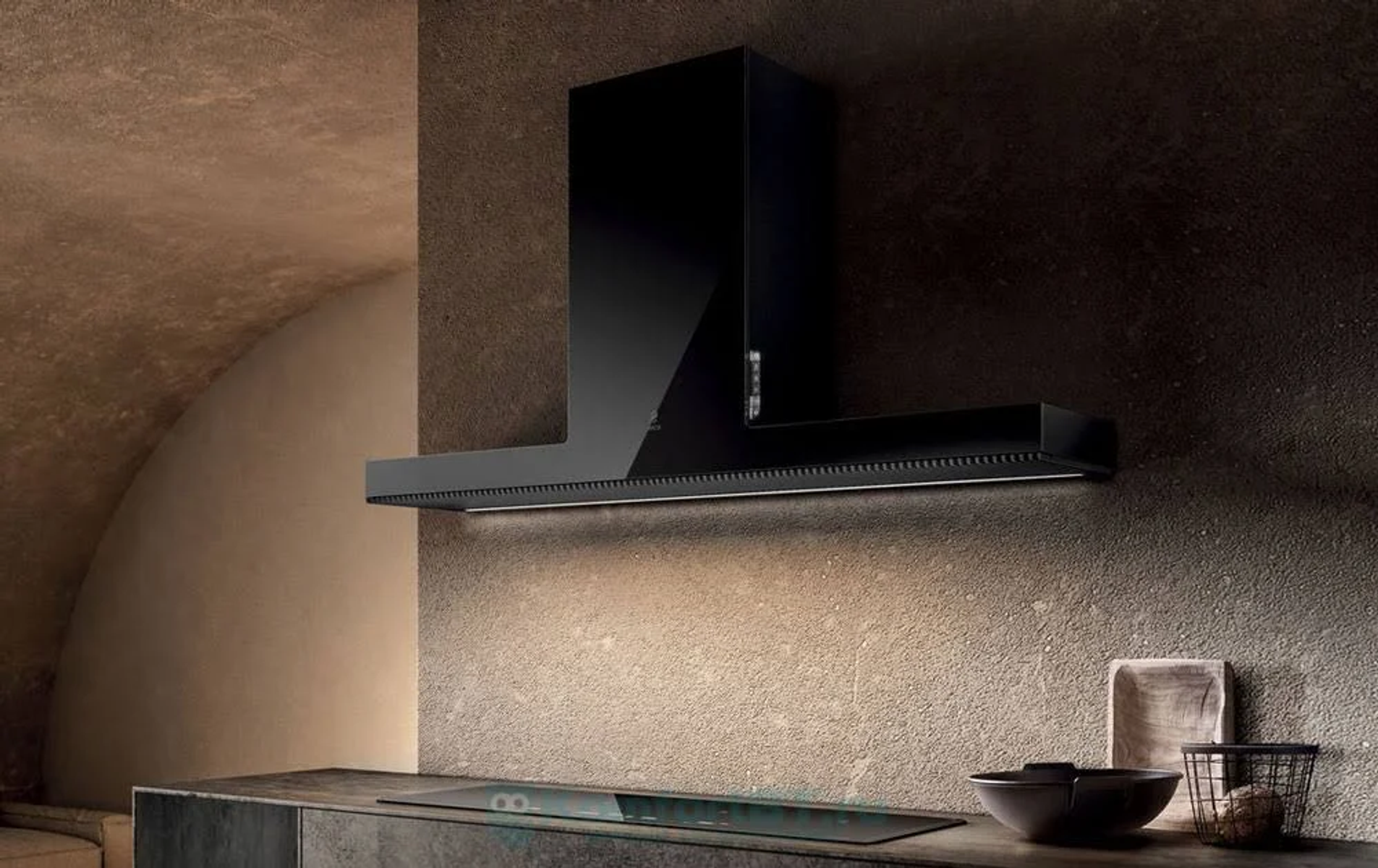 Una moderna cappa da cucina nera. La scena comprende un piano cottura, una ciotola e utensili da cucina. Lo sfondo è un muro strutturato.