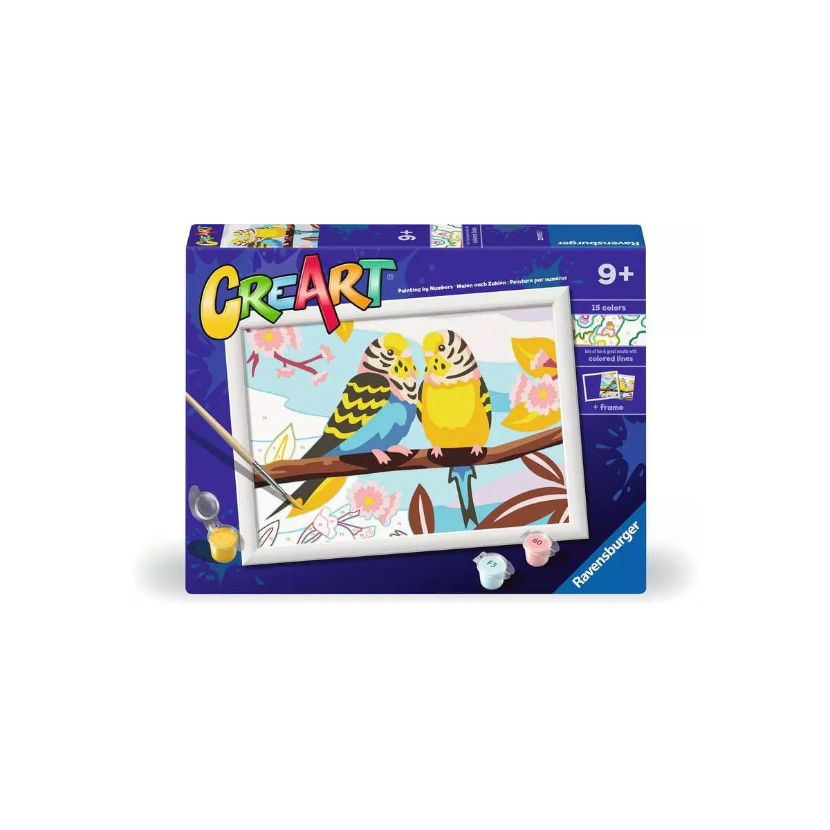 Un kit de pintura 'Creart' muestra dos periquitos en una rama. La caja es azul, tiene una clasificación de edad de 9+ y el logo de Ravensburger.