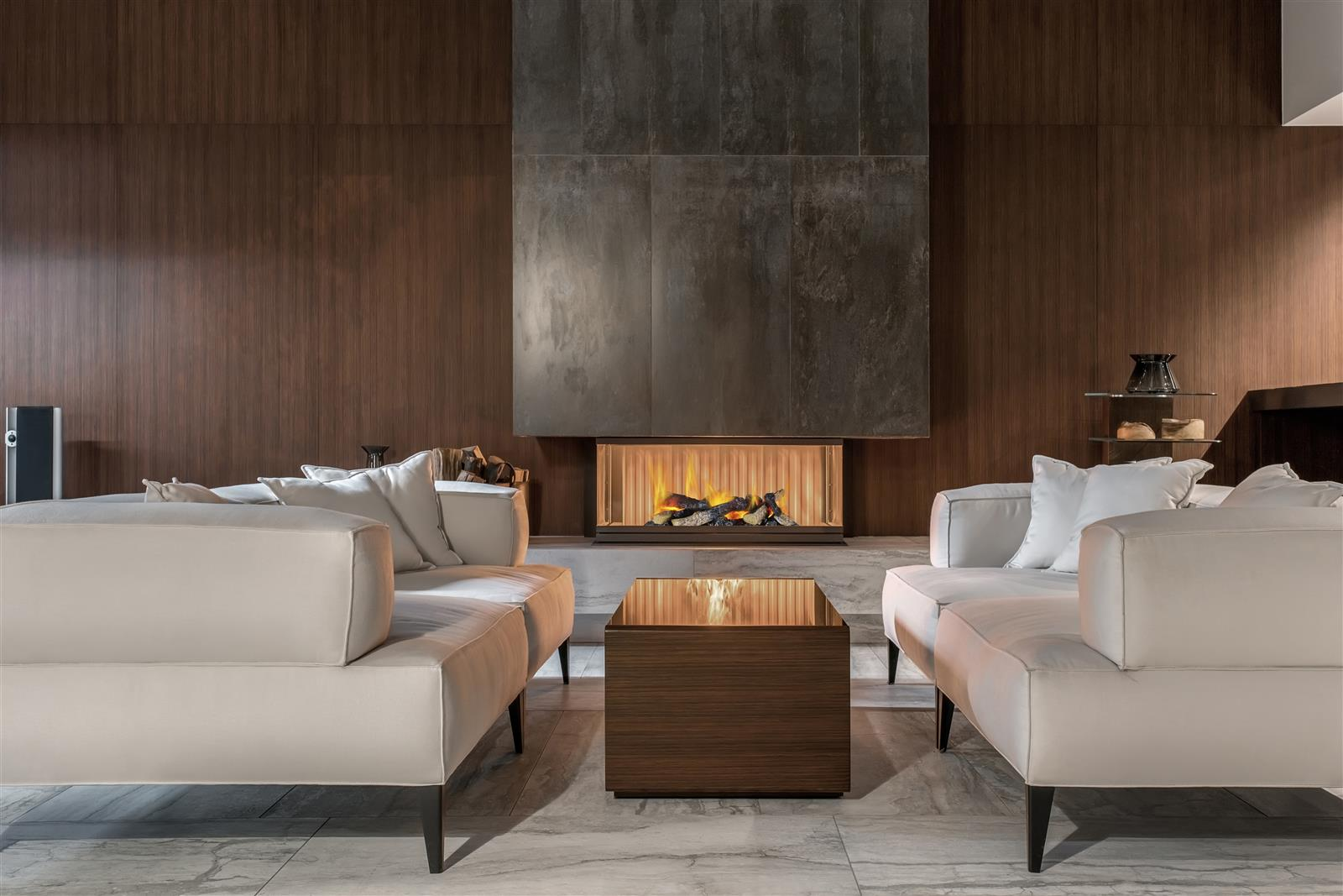 Ein modernes Wohnzimmer mit Kamin, Sofas und Couchtisch. Die Wände sind aus braunem Holz, der Boden gefliest.