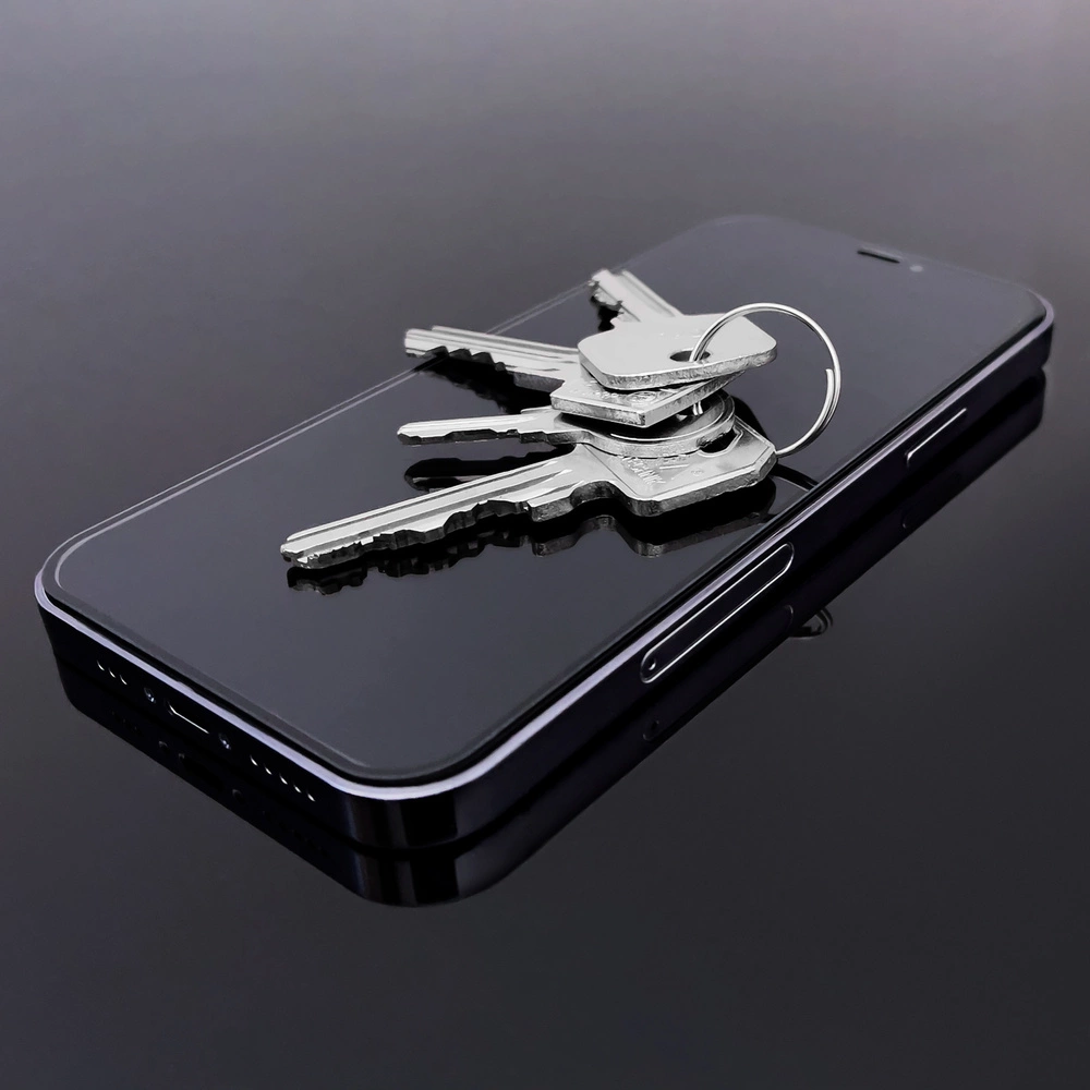 Chiavi appoggiate su uno smartphone nero su una superficie riflettente. Le chiavi sono argentate e il telefono nero. Sfondo scuro.