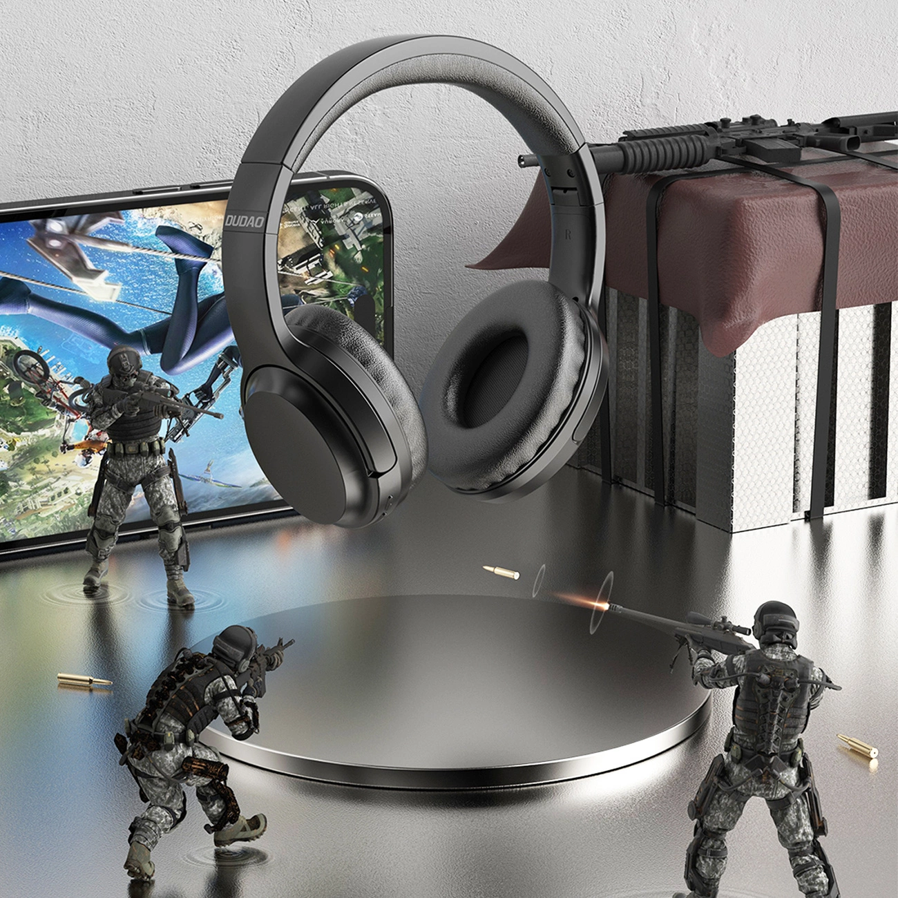 Czarne słuchawki spoczywają z telefonem wyświetlającym scenę gry z żołnierzami. Zabawkowe żołnierze i kule są rozrzucone wokół słuchawek.