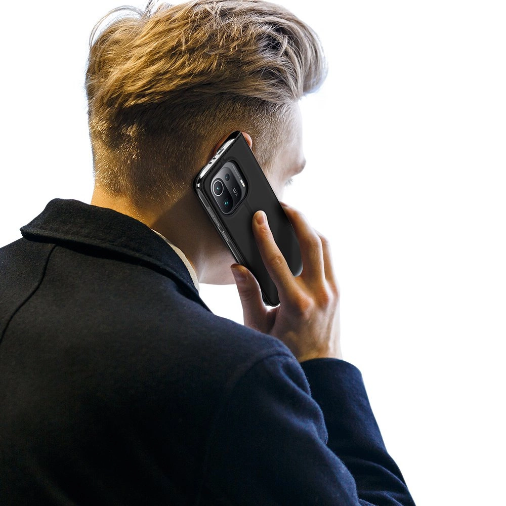 Un uomo con i capelli biondi tiene uno smartphone nero all'orecchio. Indossa un cappotto scuro. Lo sfondo è bianco.