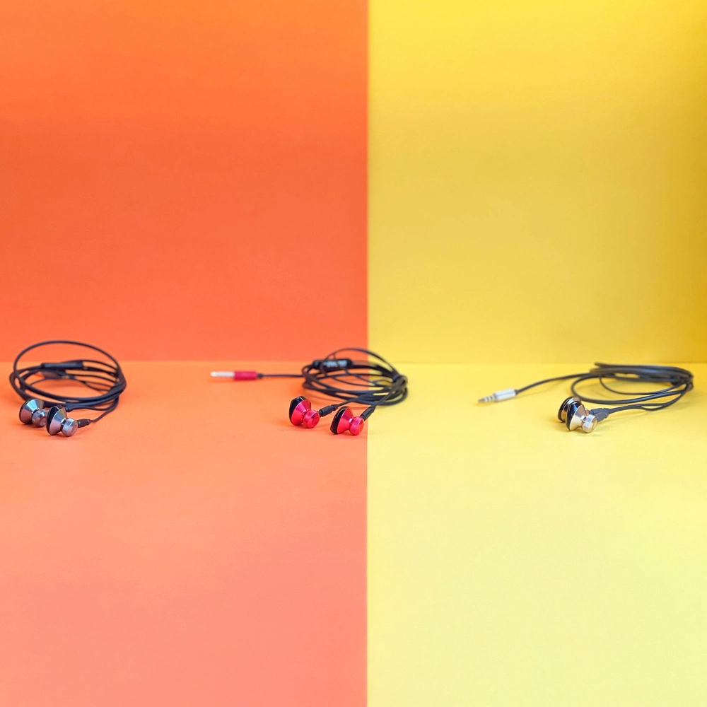 Trzy zestawy przewodowych słuchawek na kolorowym tle. Jeden zestaw jest srebrny, drugi czerwony, a ostatni złoty, każdy z czarnymi kablami.