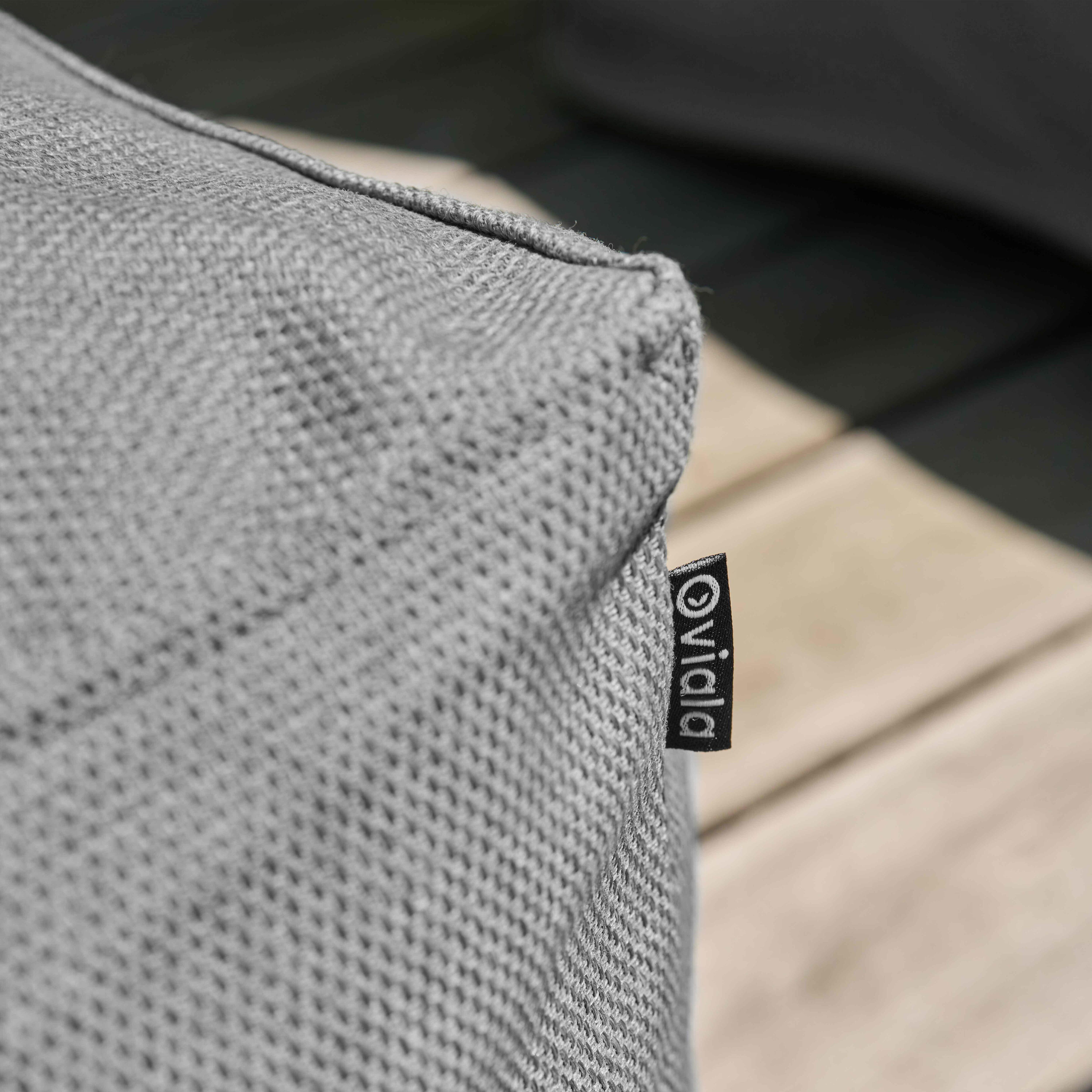 Nahaufnahme eines grauen Stoffes. Ein schwarzes Etikett mit weißem Text 'Vida' ist befestigt.