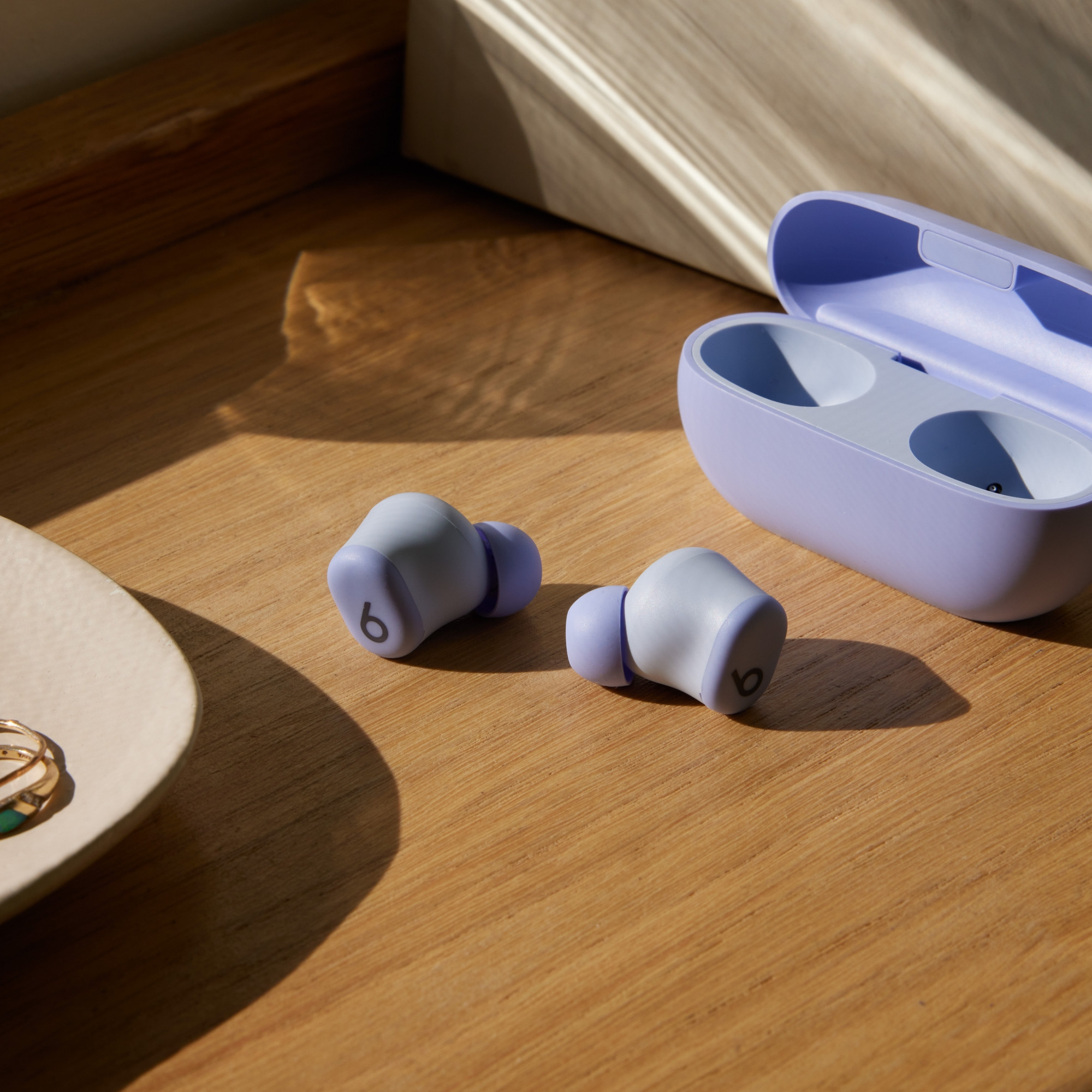 Słuchawki, etui i akcesoria na drewnianej powierzchni. Słuchawki białe i fioletowe. Etui otwarte. Pierścionki na talerzu.