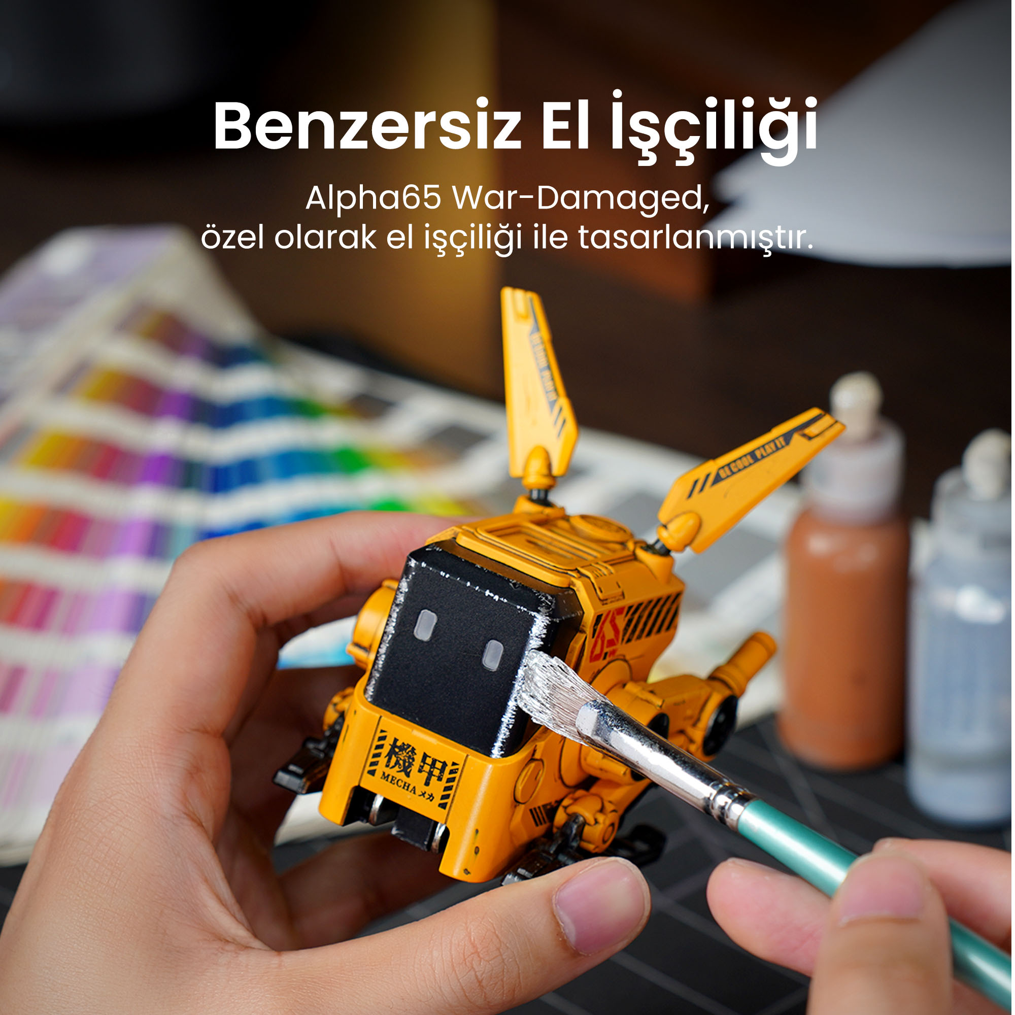 Bir kişi sarı bir oyuncak robotu fırçayla boyuyor. Arka planda boya şişeleri ve bir renk paleti var.
