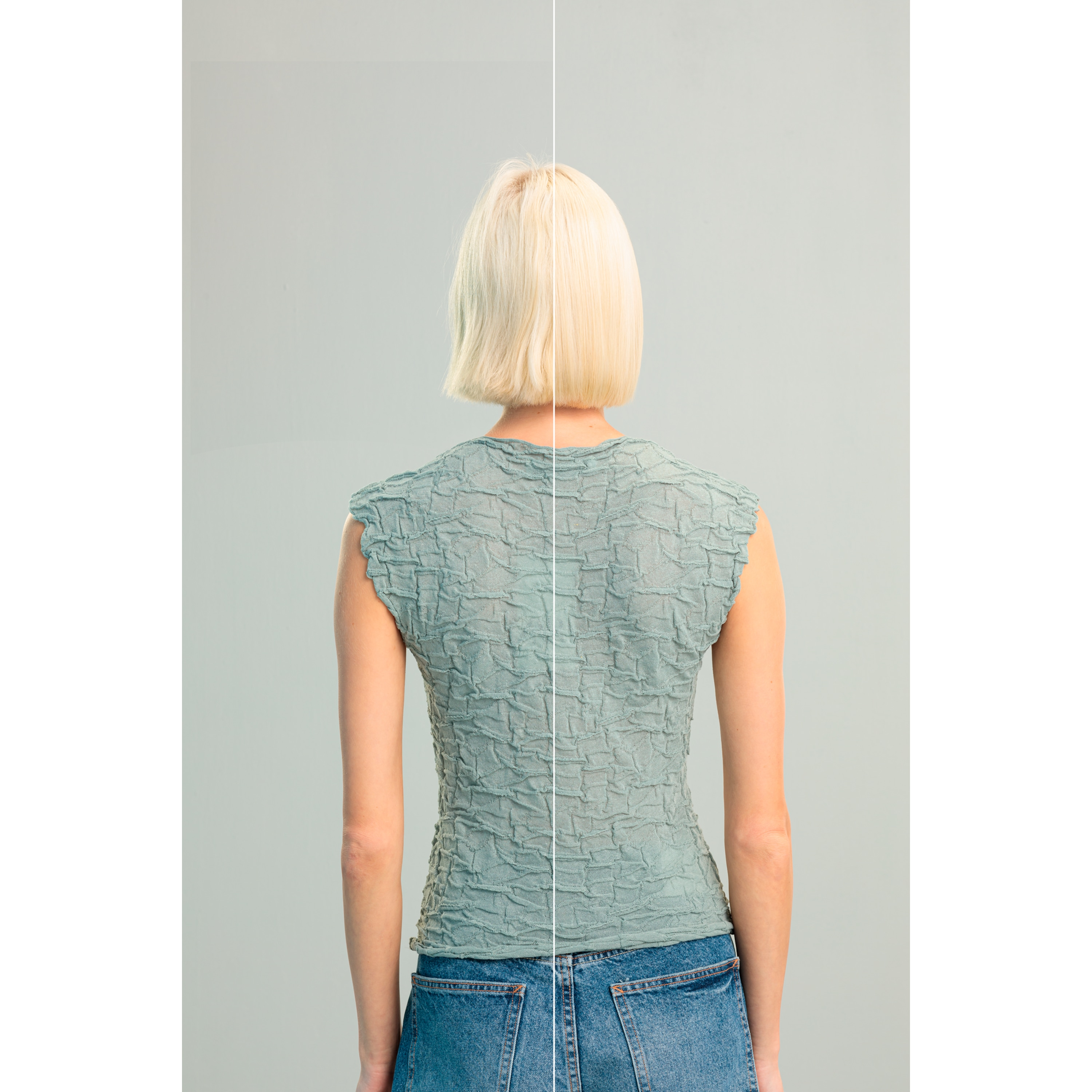 Widok z tyłu kobiety w zielonym topie i niebieskich dżinsach, z krótkimi blond włosami na szarym tle.