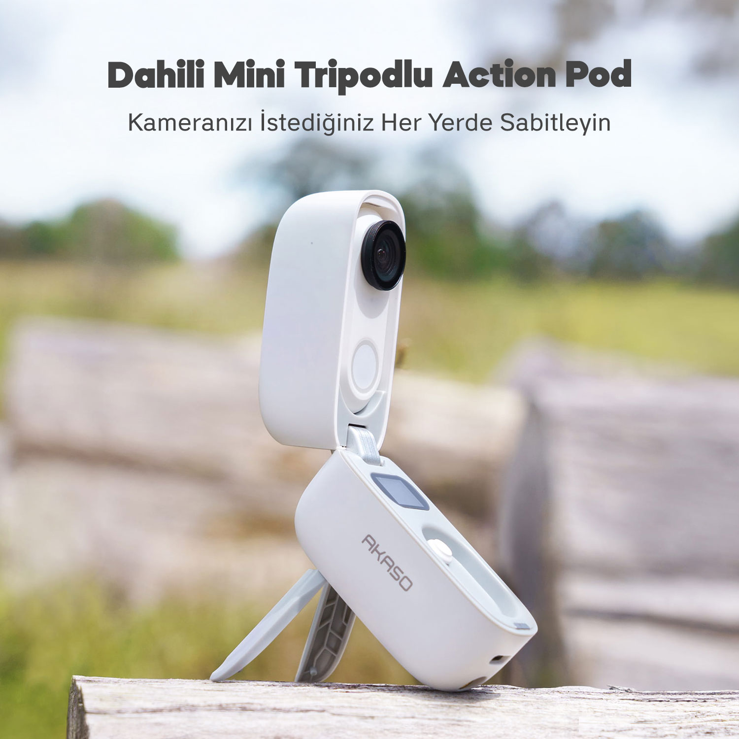 Ahşap yüzey üzerinde beyaz bir Akaso Action Pod, tripodlu. Arka planda yeşil çimenler ve ağaçlar var.