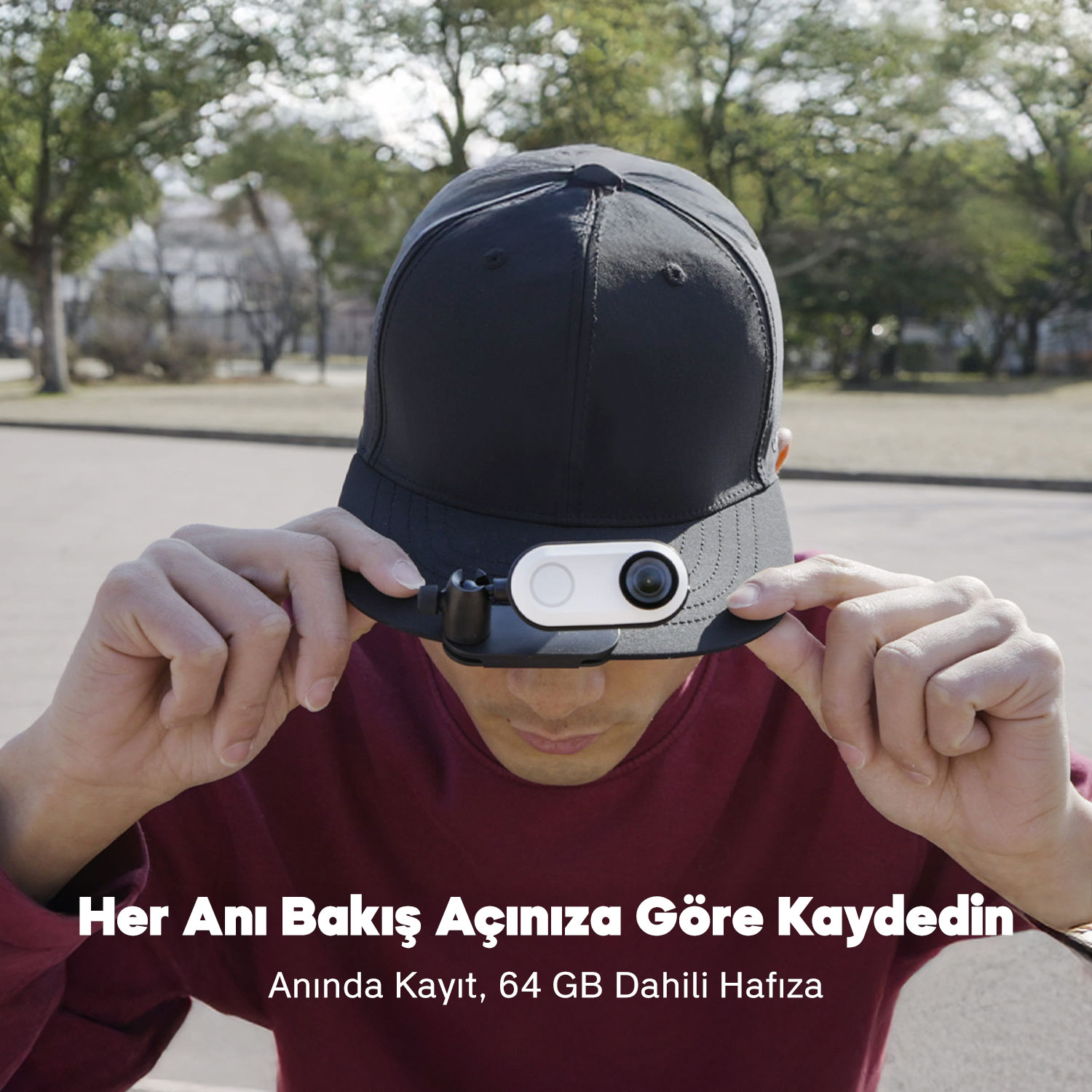 Kamerası olan siyah bir şapka takan bir kişi. Kişi şapkayı tutuyor. Arka planda ağaçlar ve metin var.