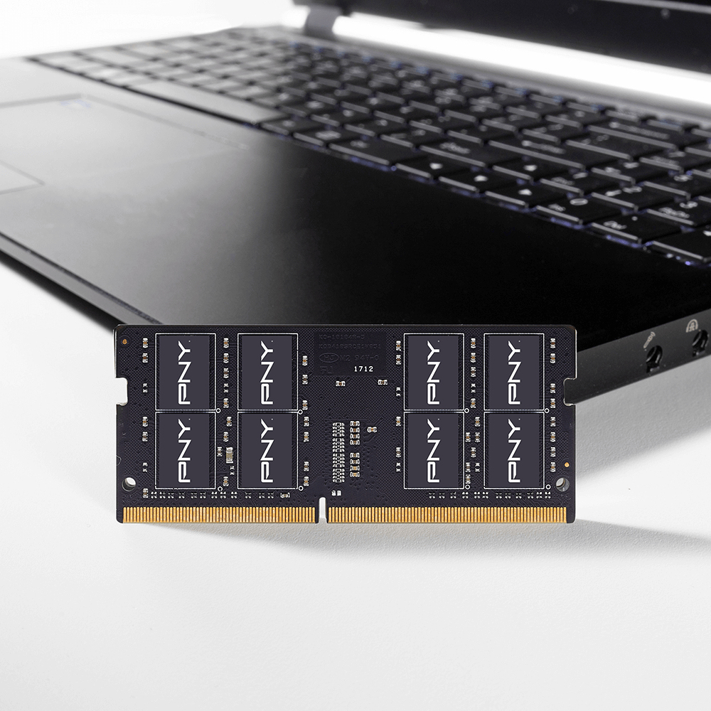 Un modulo RAM con logo PNY davanti a un laptop. La RAM è nera con connettori dorati. Il laptop è nero.