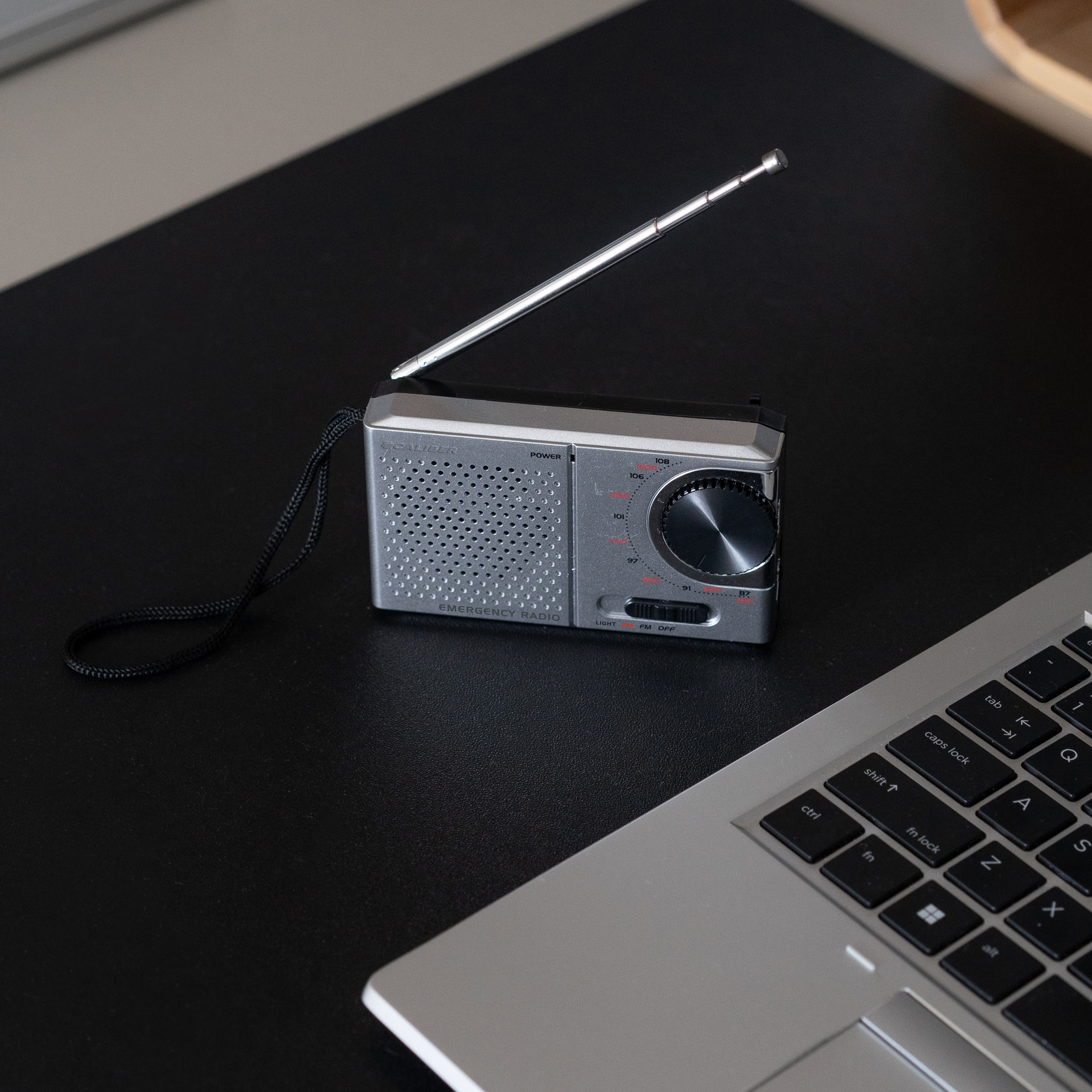 Een zilveren radio met antenne en een laptop op een zwart oppervlak.