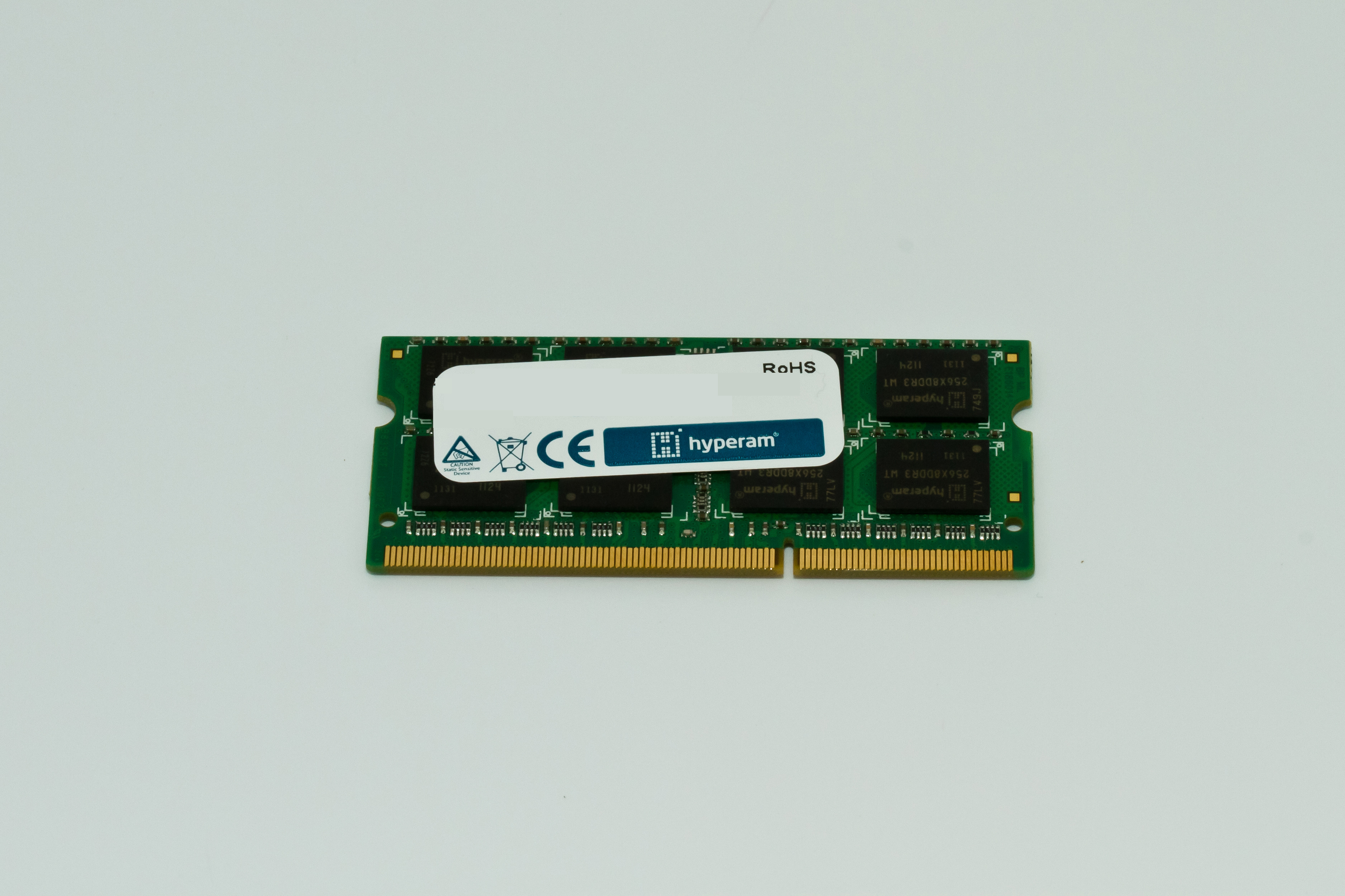 Un modulo RAM verde con pin dorati, etichetta bianca e testo nero, su sfondo bianco.