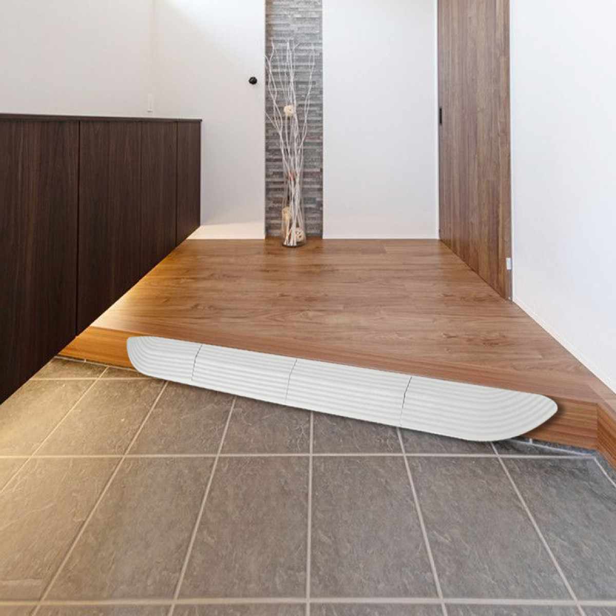 Korytarz z drewnianą podłogą i białą rampą. W tle wazon z gałęziami. Po lewej stronie ciemne drewniane szafki.