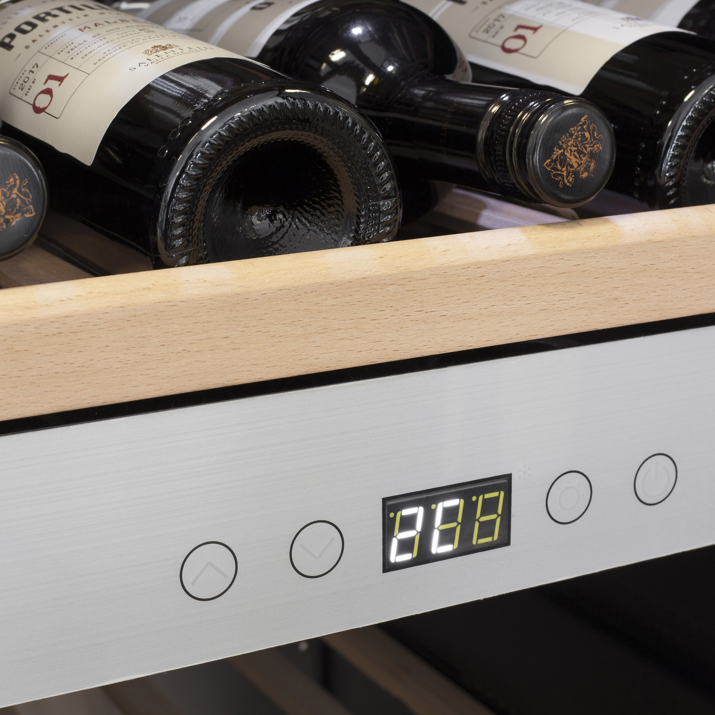 Wein wird in einem Weinkühler gelagert. Ein digitales Display zeigt die Temperatur an. Holzregal und Metalloberfläche sind sichtbar.