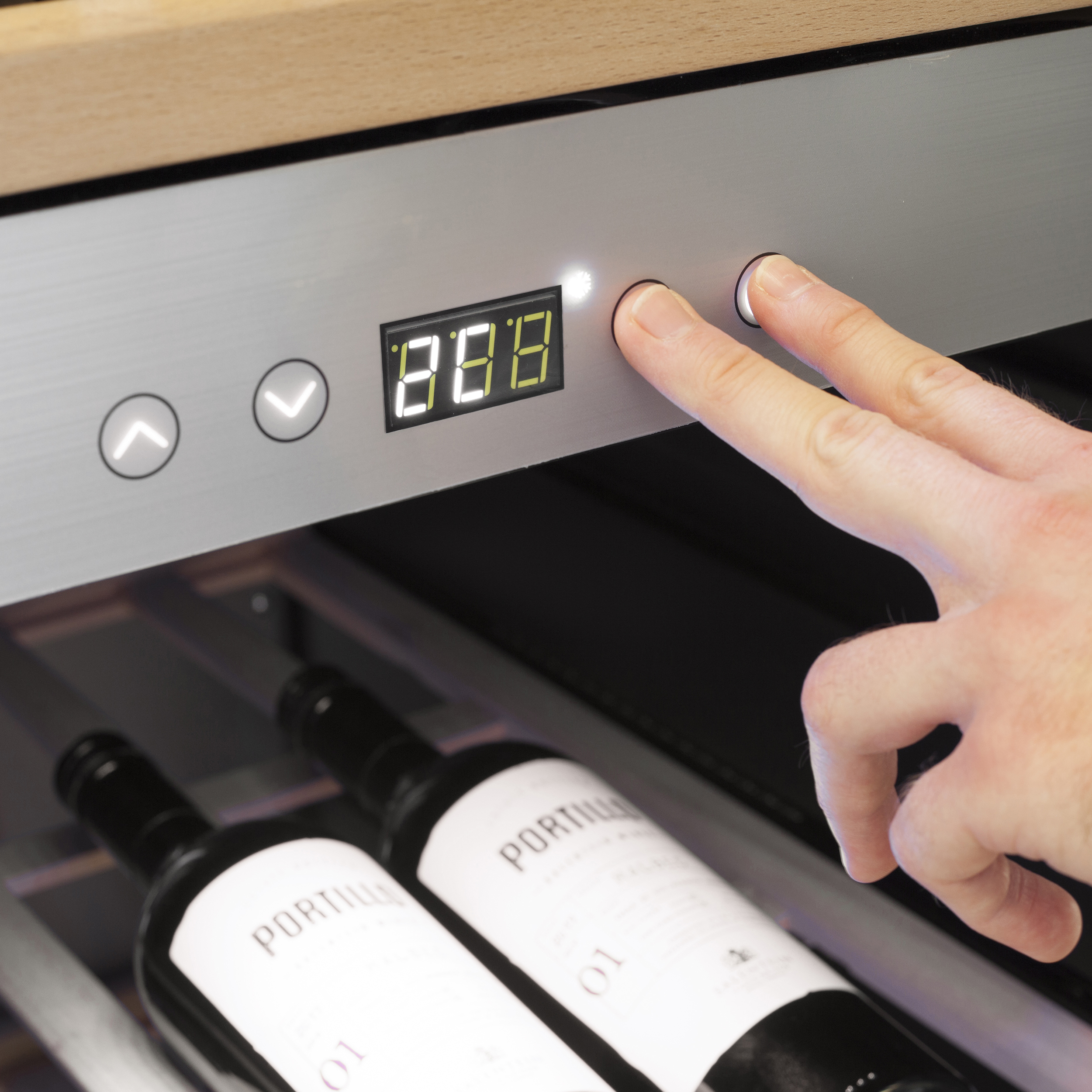Eine Hand betätigt Tasten an einem Weinkühlschrank. Weinflaschen sind unterhalb des Bedienfelds sichtbar.