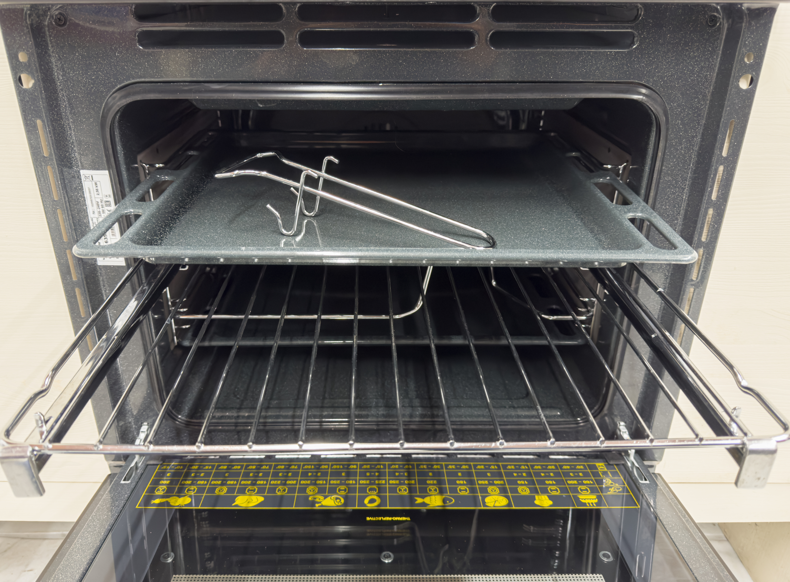 Offener Backofen mit Blech und Rost. Silberne Zangen liegen auf dem Blech. Bedienfeld unten.