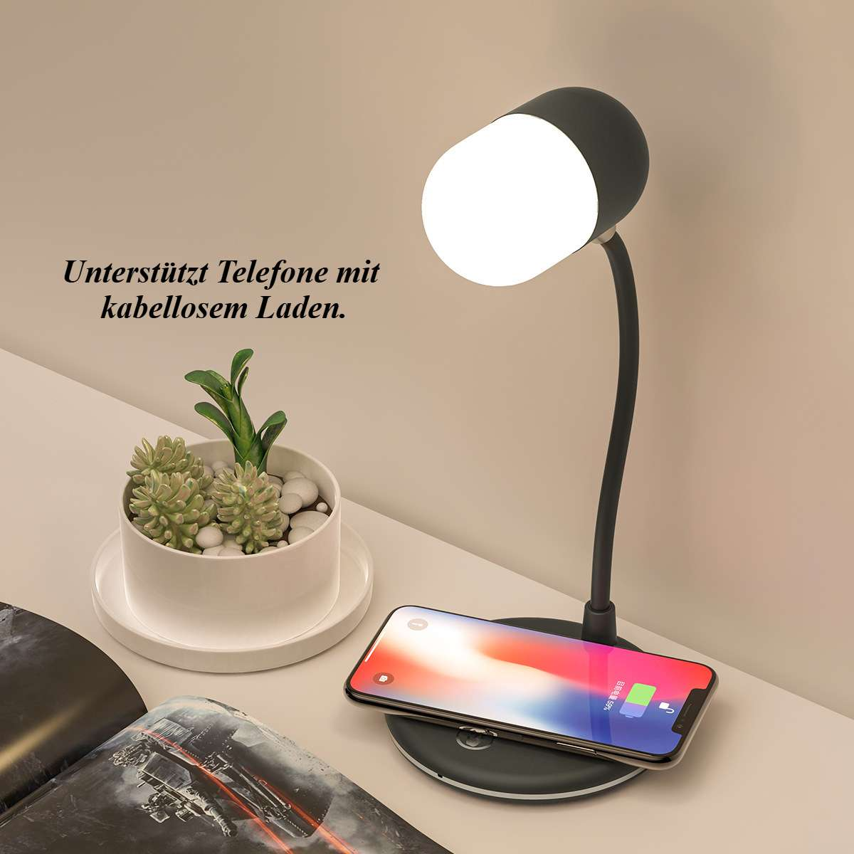 Ein Schreibtisch mit Lampe, Telefonladung und einer kleinen Topfpflanze. Das Telefon wird kabellos geladen.